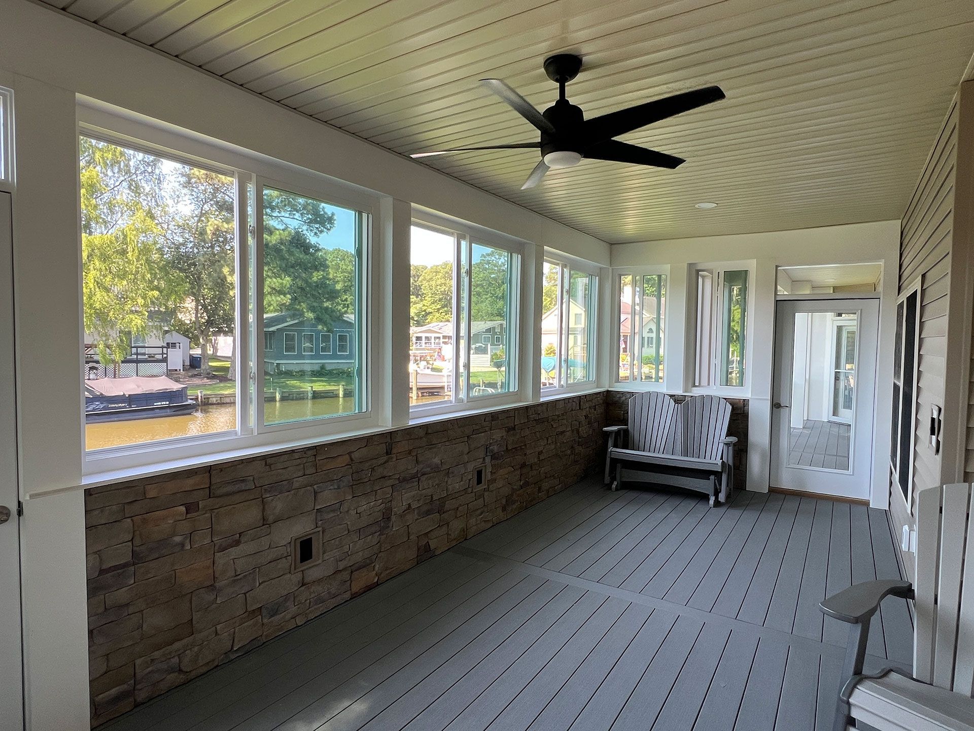 Sunroom overlooking water, with stone wall, windows, and a bench.