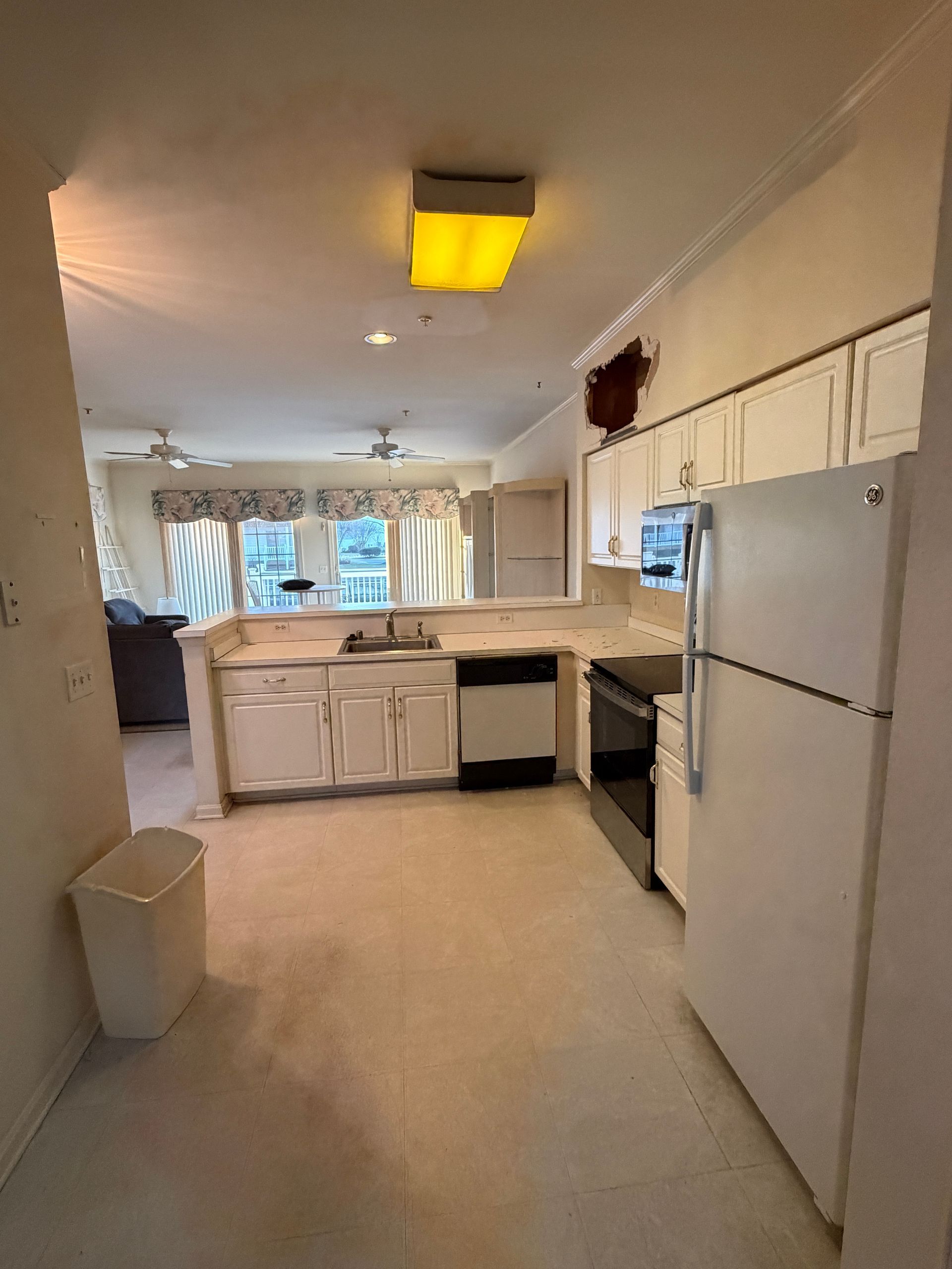 Bright kitchen with white cabinets, refrigerator, stove, and a window with curtains in the background