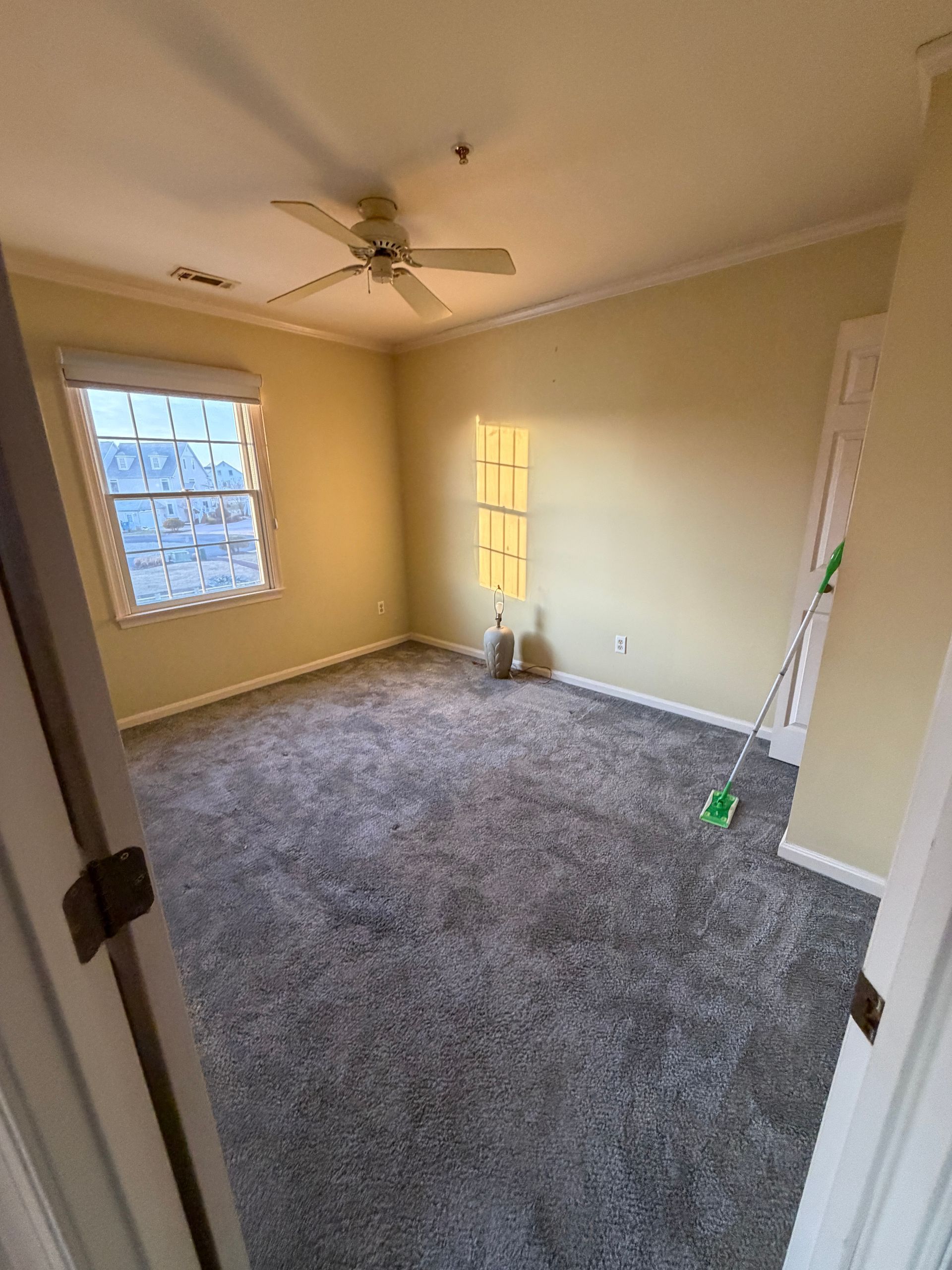 Empty beige bedroom with gray carpet, ceiling fan, and two windows.