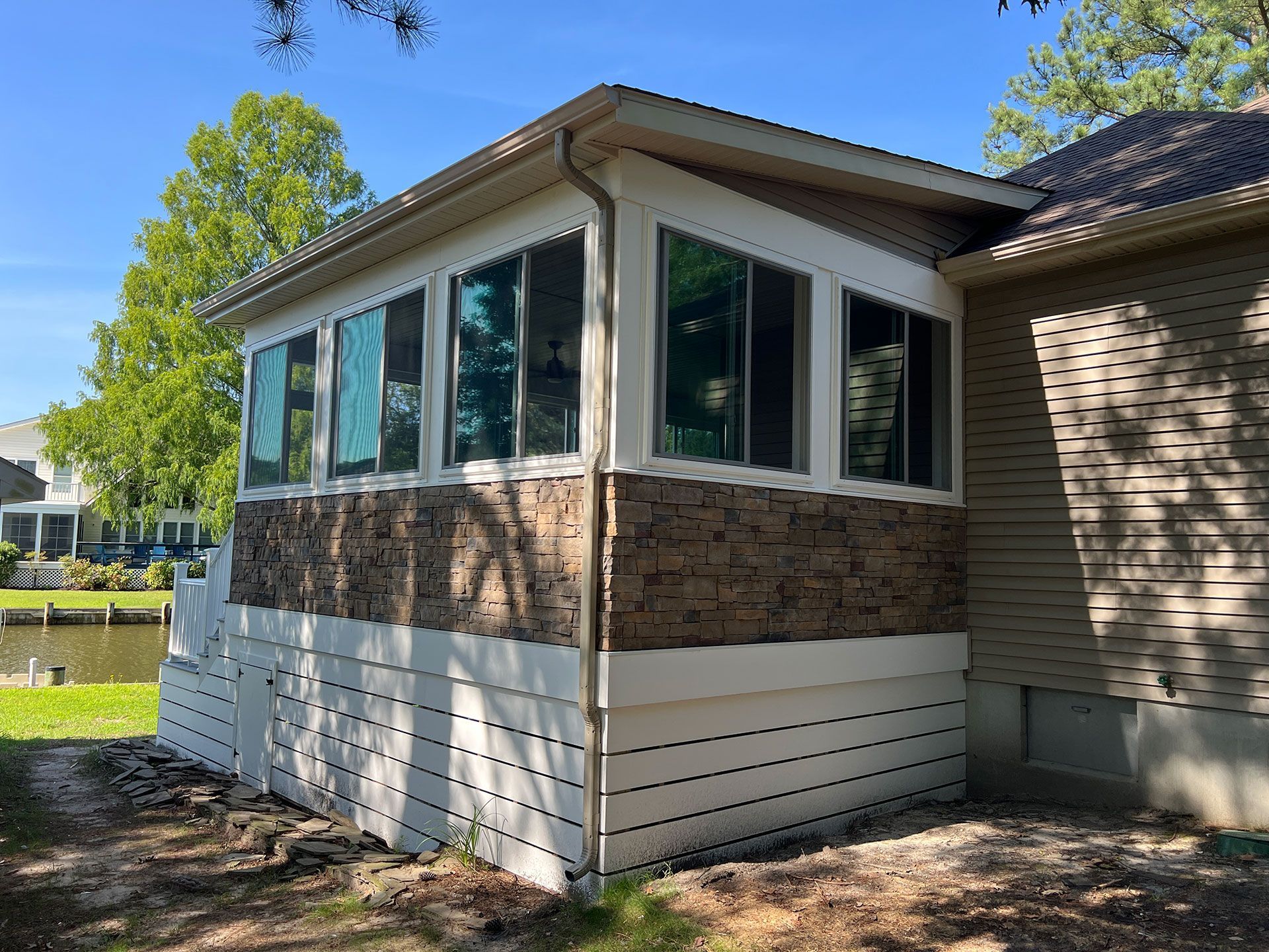 Screened porch with stone veneer and white siding attached to a house near water.