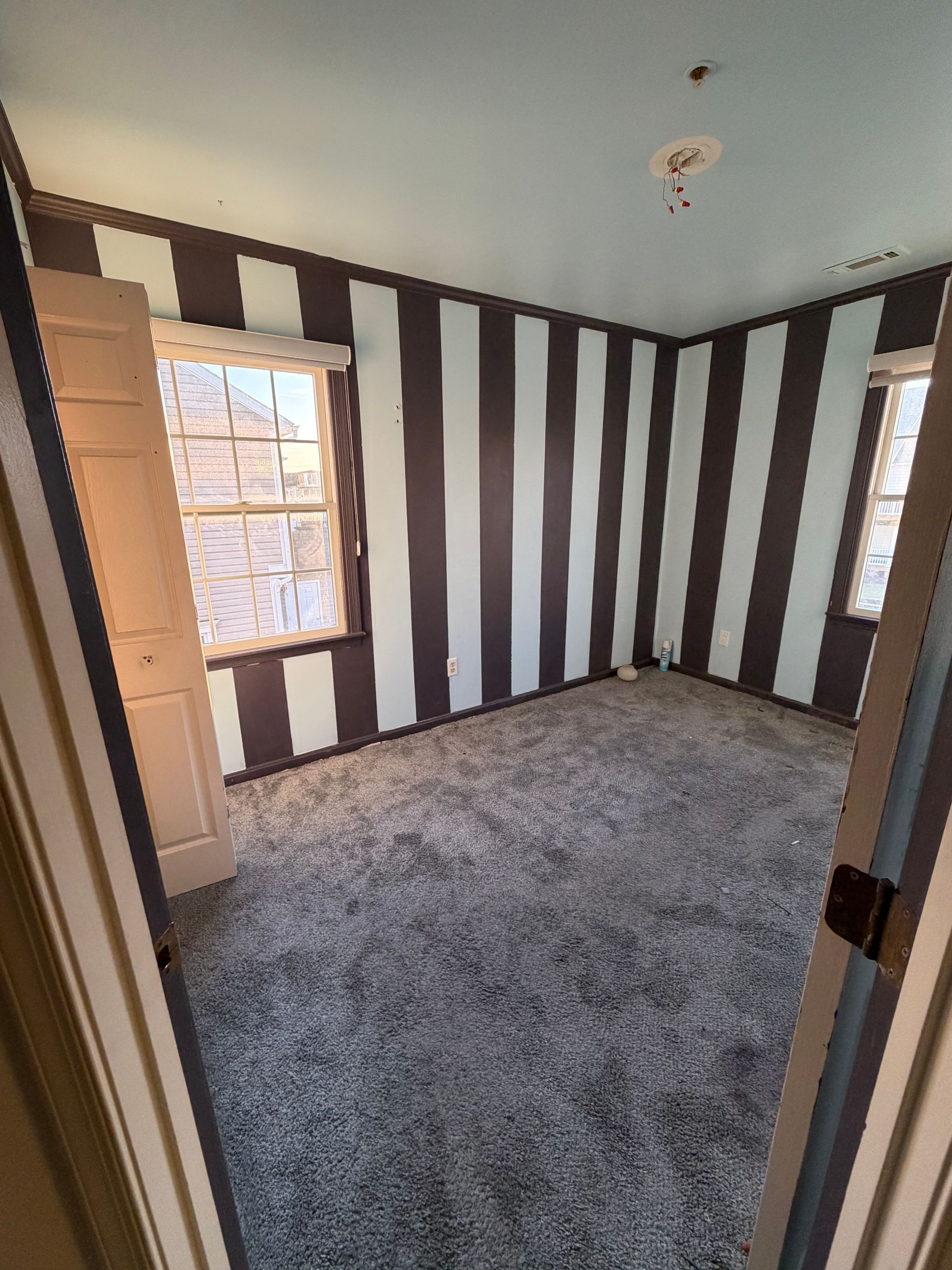 Empty room with striped brown-and-white walls, gray carpet, and two windows.