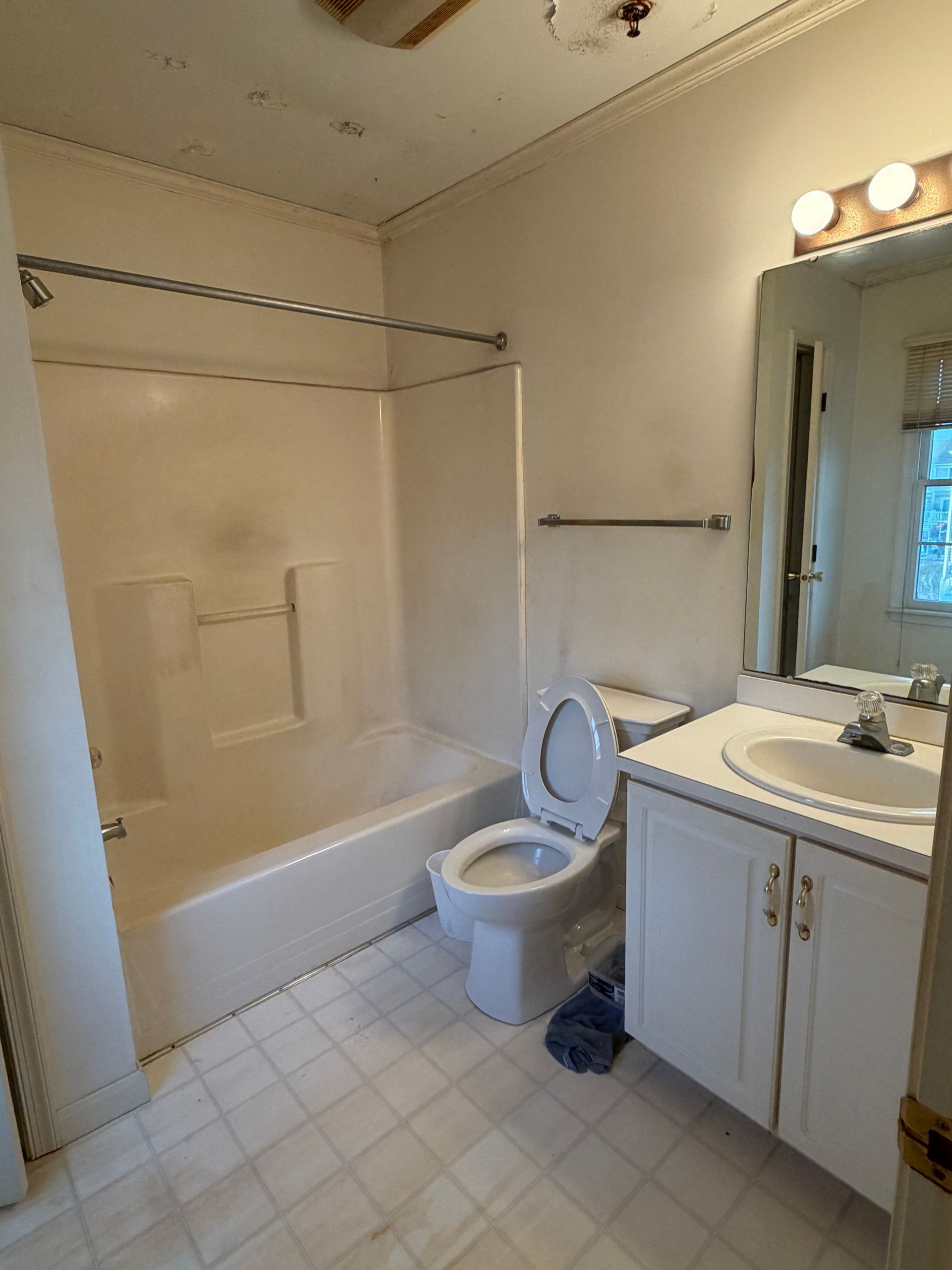 Small bathroom with tub, toilet, and vanity with mirror lights.
