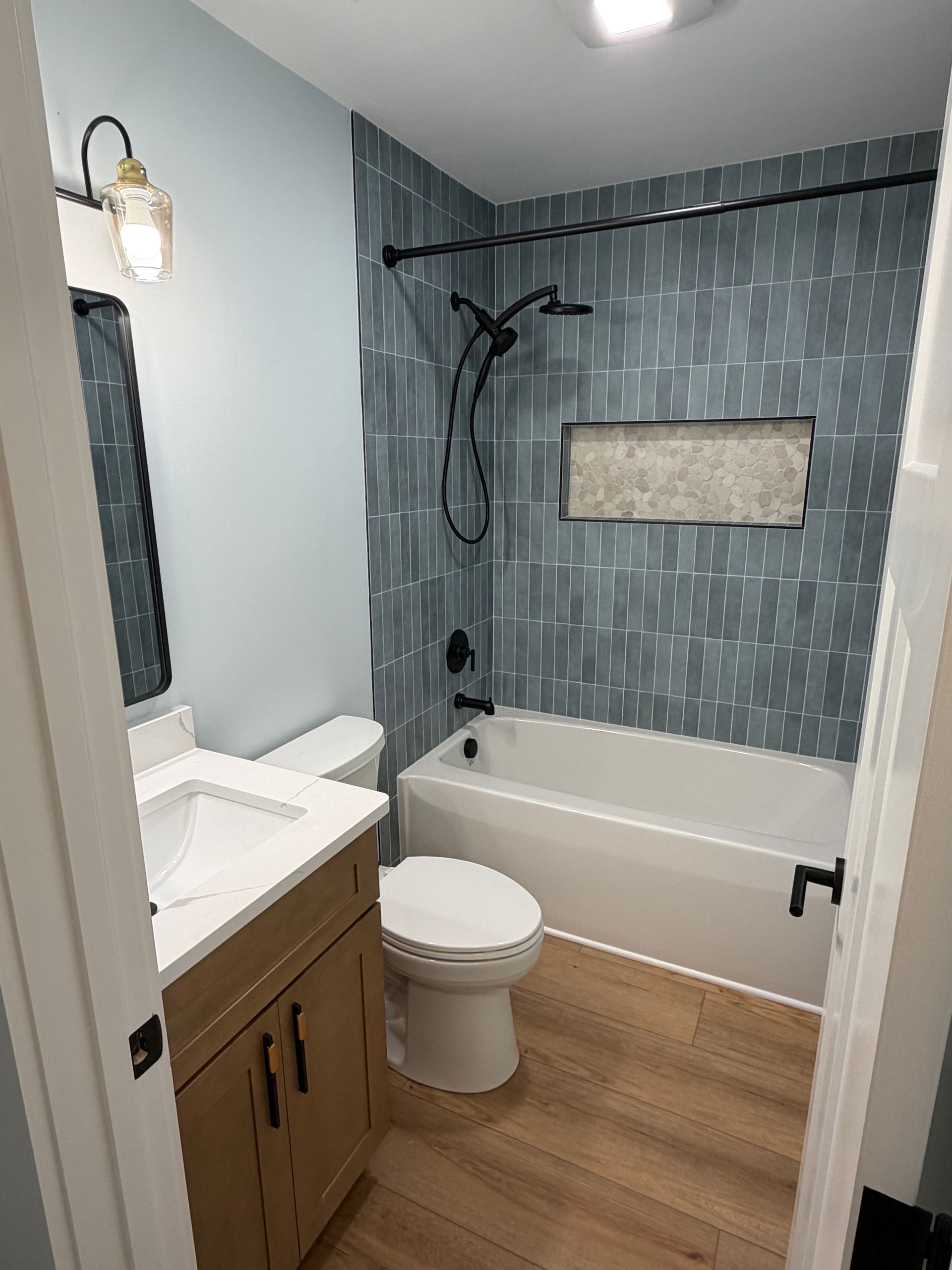 Modern bathroom with vanity, toilet, bathtub, and blue tiled shower wall.