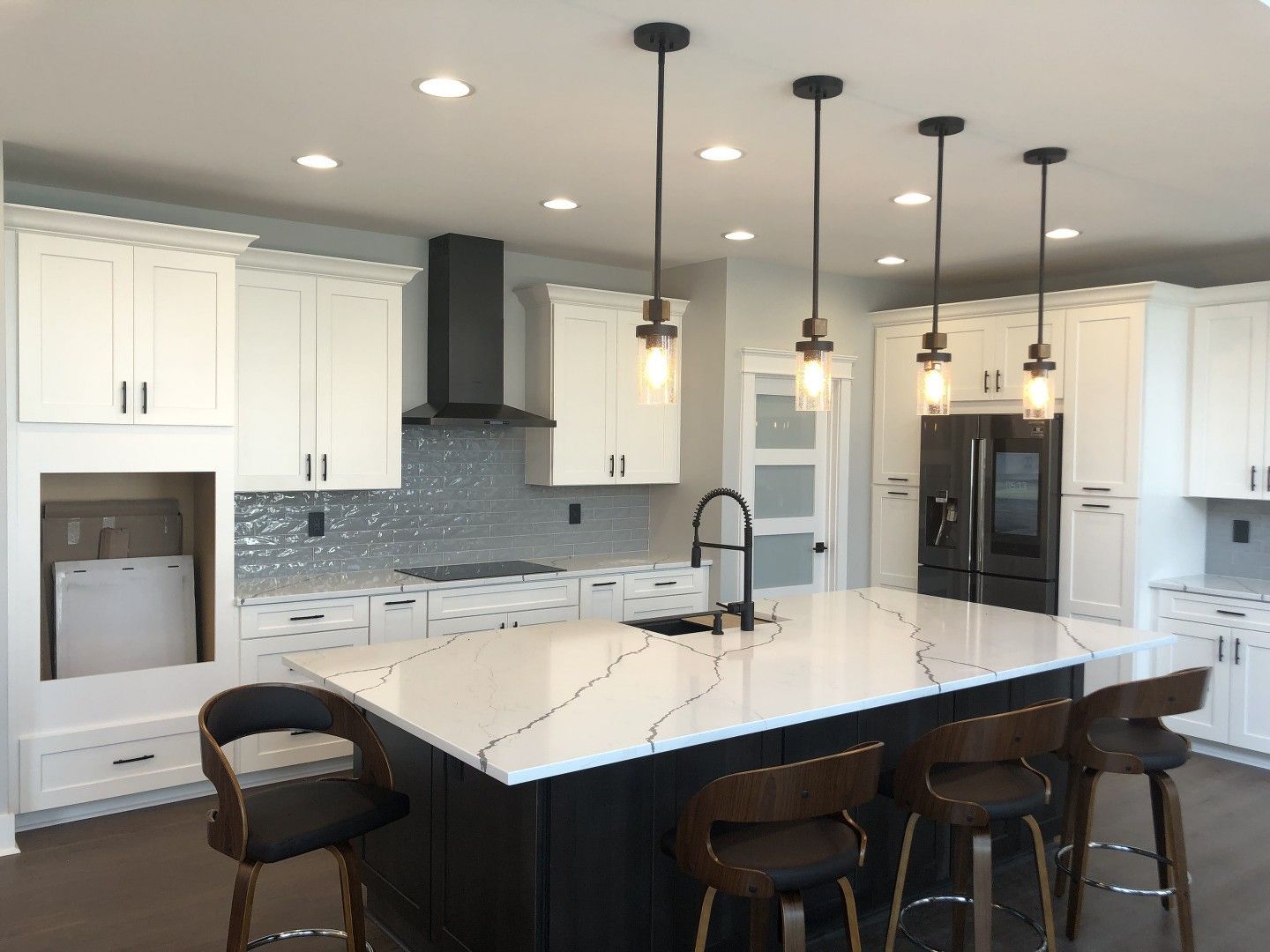 A kitchen with white cabinets , a large island , and stools.