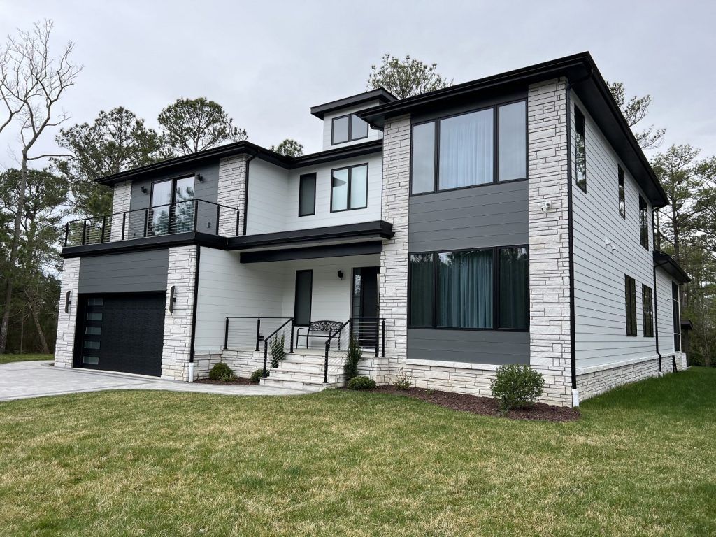 A large white and gray house with a black garage is sitting on top of a lush green lawn.