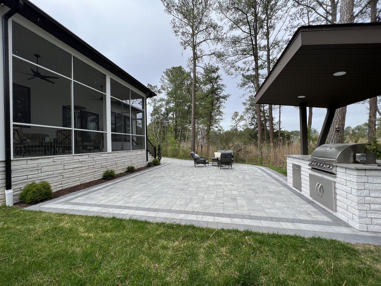 A patio with a grill and a screened in porch next to a house.
