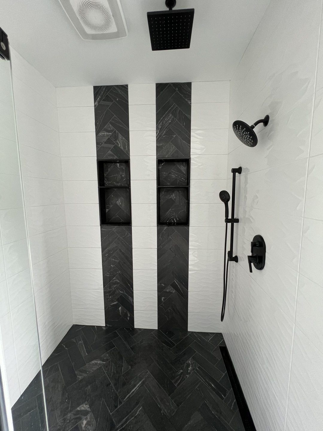 A shower with black and white tiles and a black shower head.
