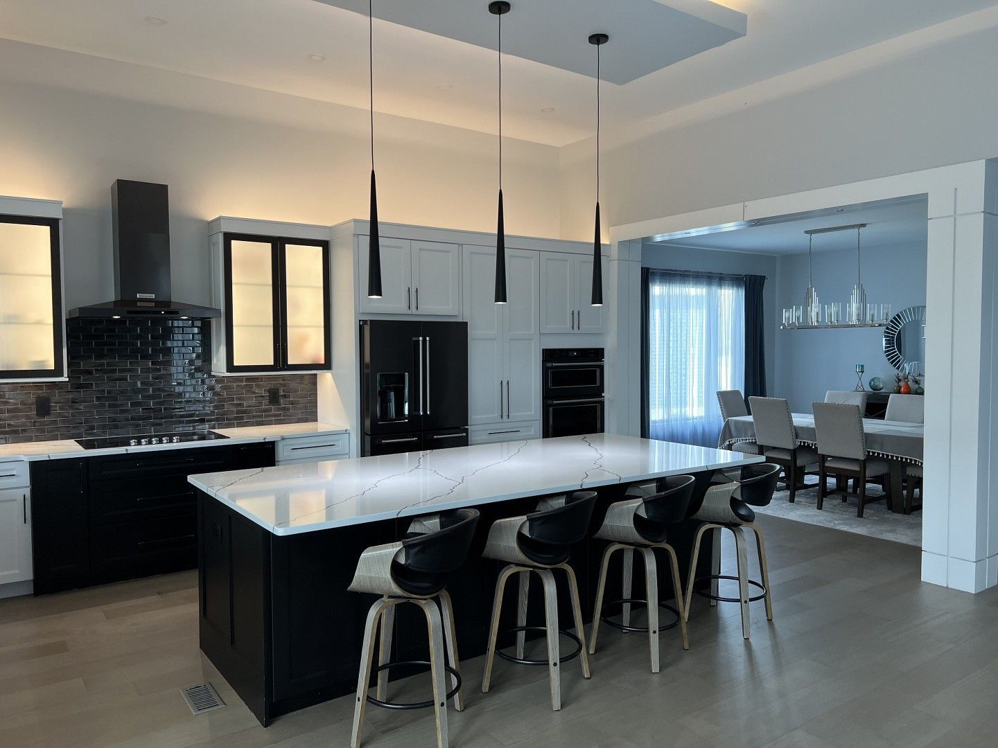 A kitchen with a large island and stools and a dining room in the background.