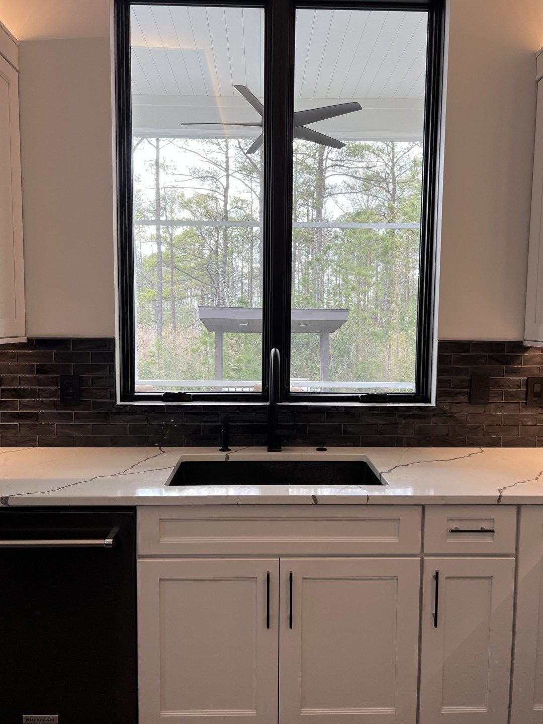 A kitchen with a sink and a window with a ceiling fan.