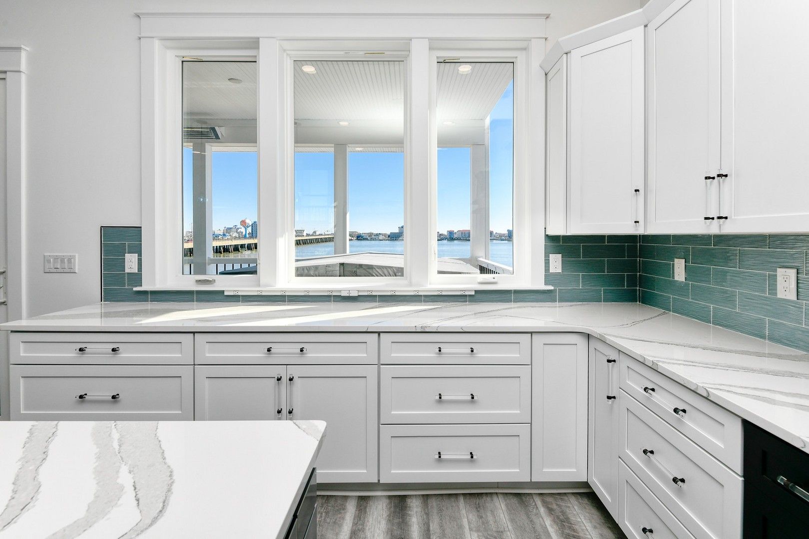A kitchen with white cabinets , white counter tops , and a large window.