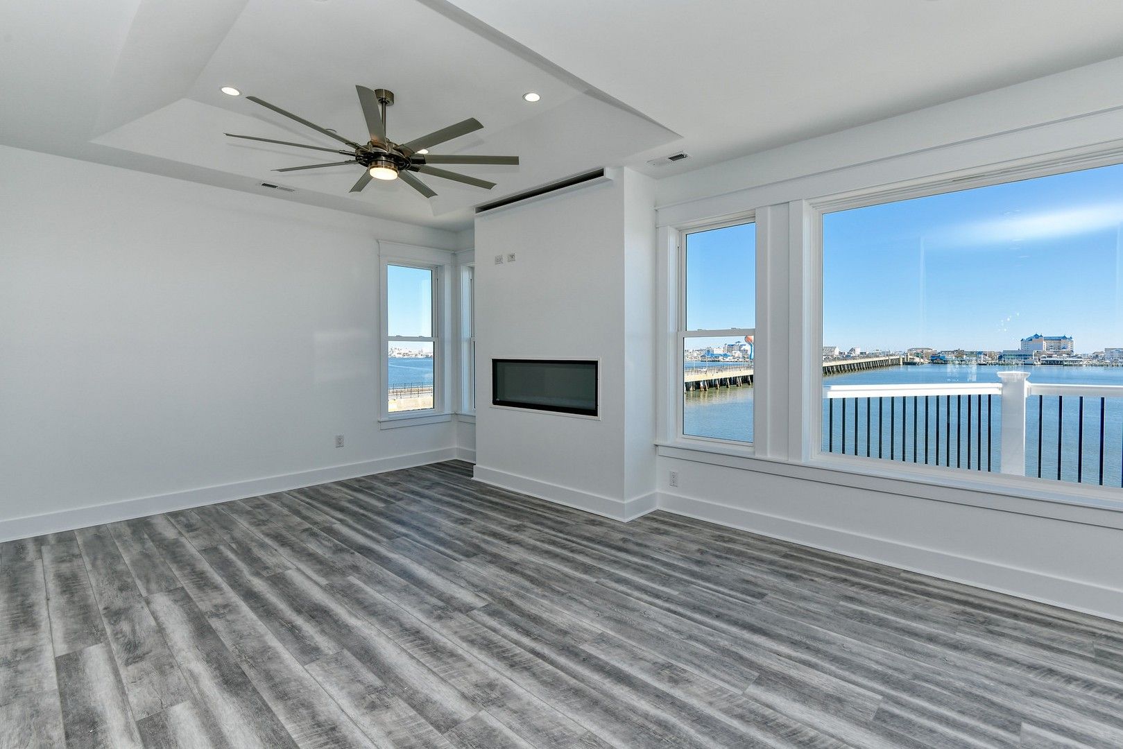 An empty living room with a ceiling fan and a view of the ocean.
