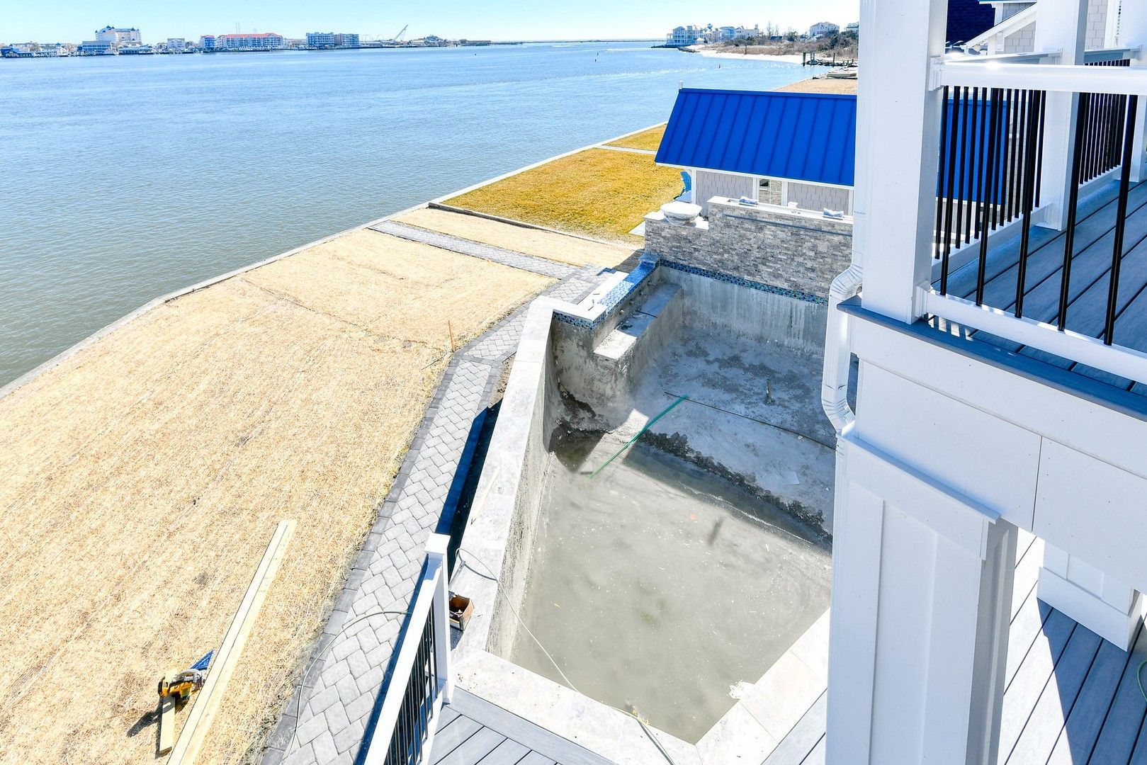 A white house with a blue roof sits on a beach next to a body of water.