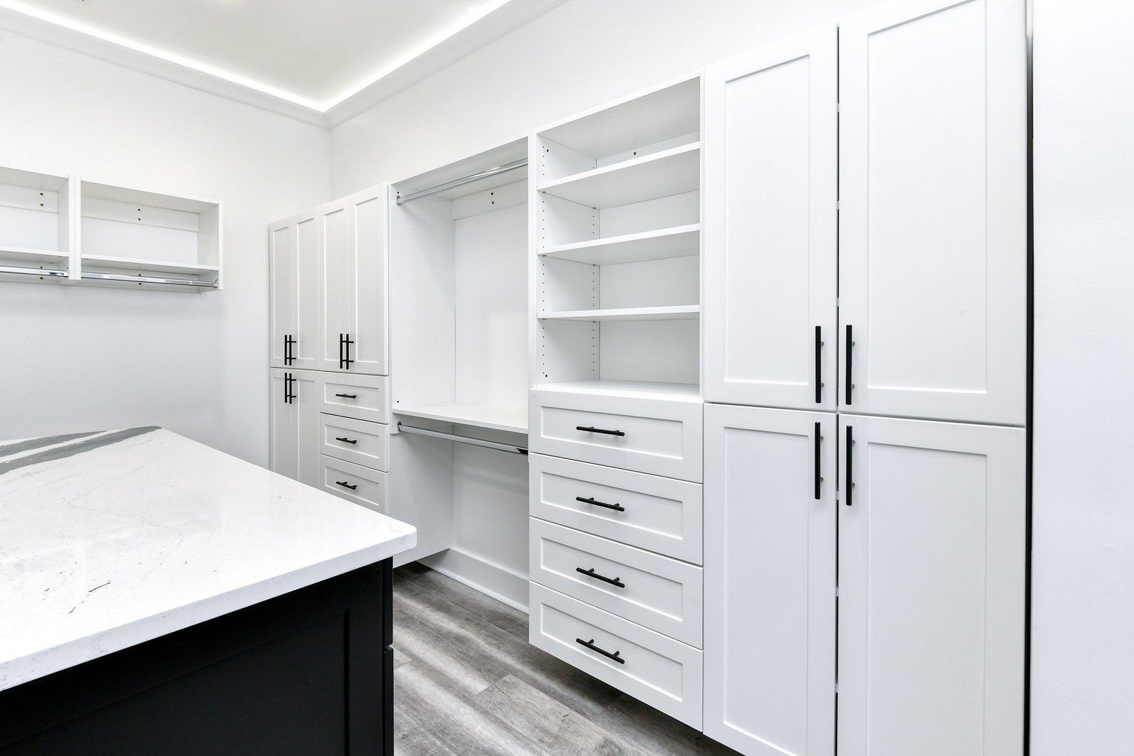 A walk in closet with white cabinets , drawers , and shelves.