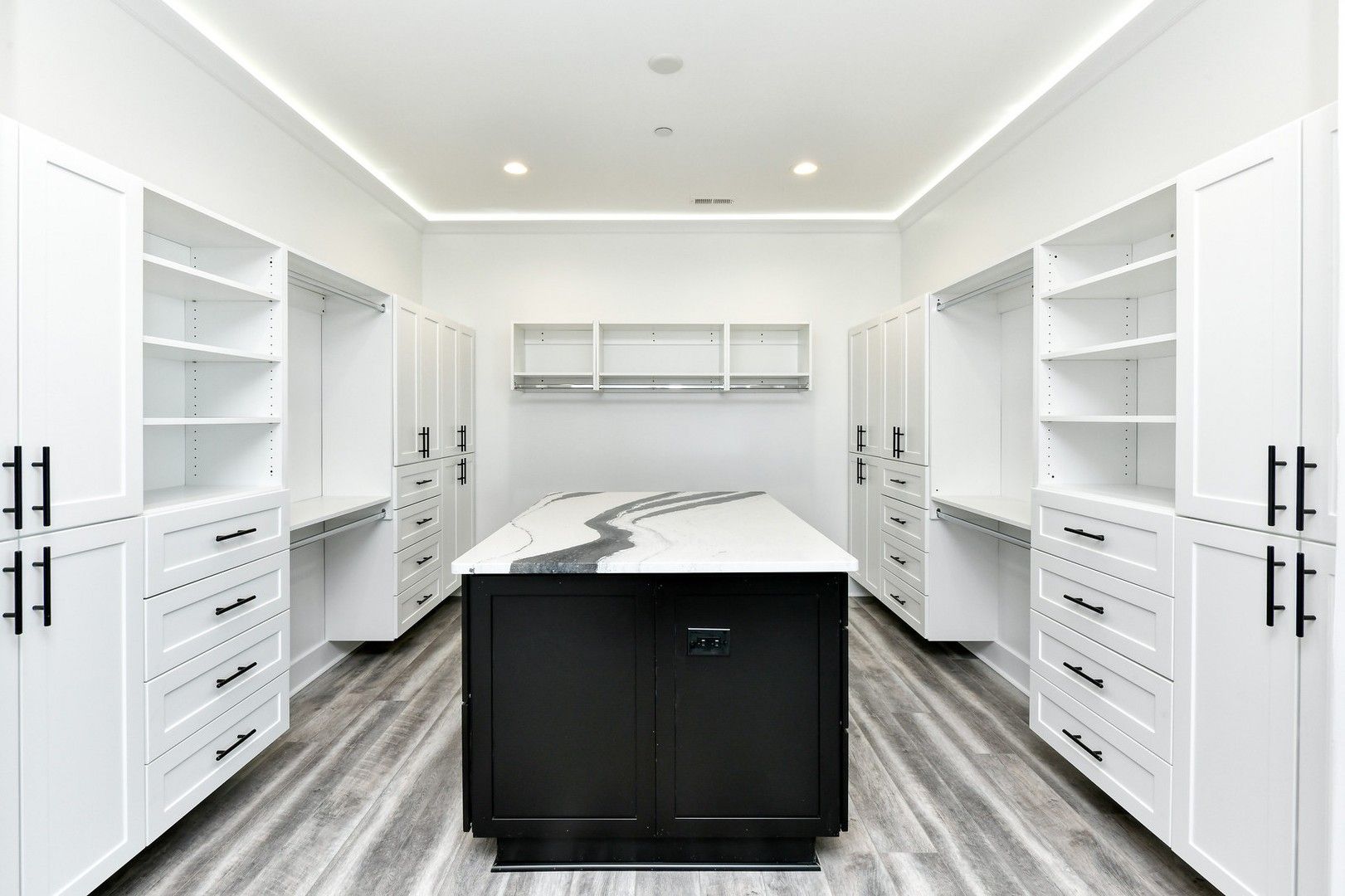 A large walk in closet with white cabinets and a black island in the middle.