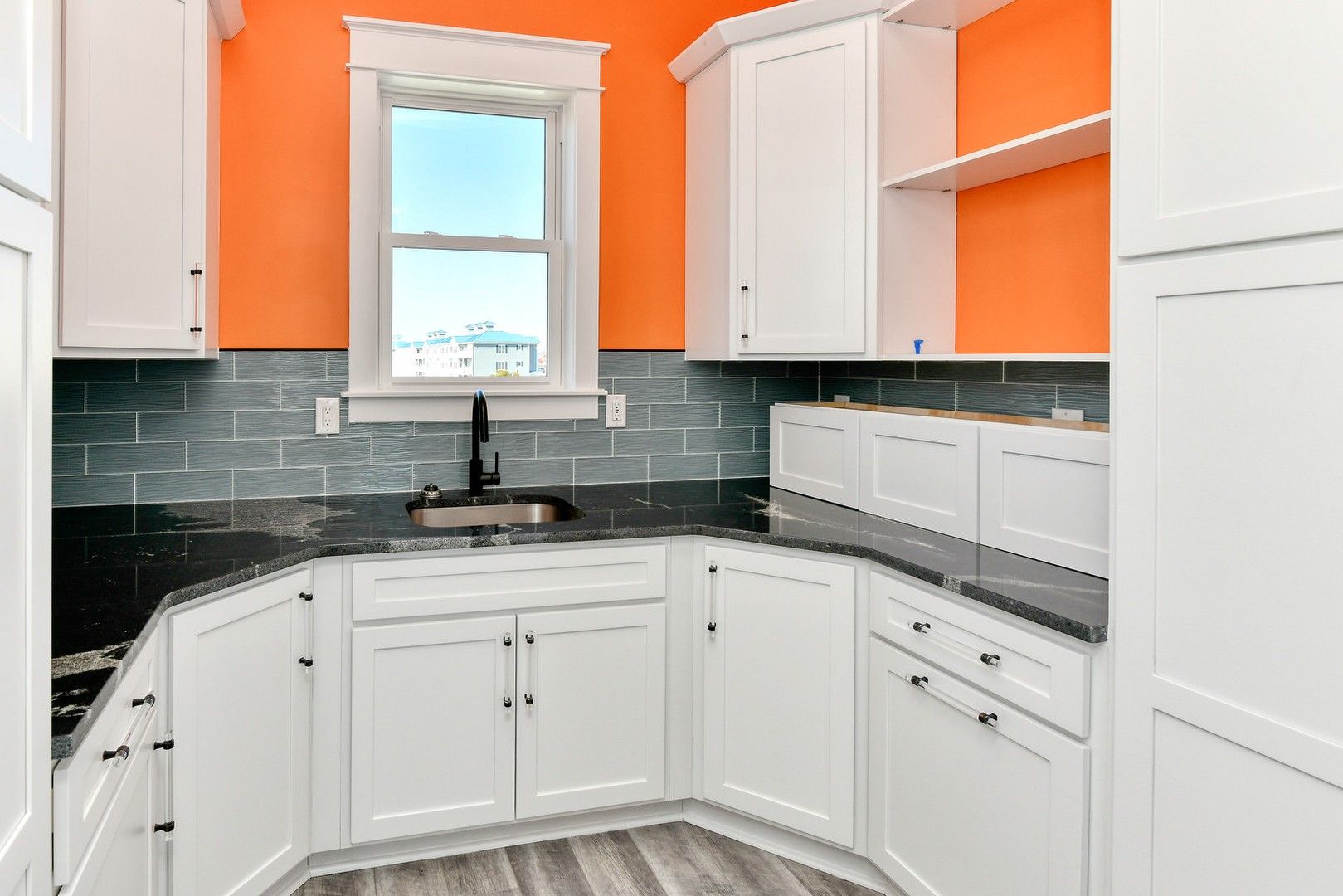A kitchen with white cabinets , black counter tops , and orange walls.