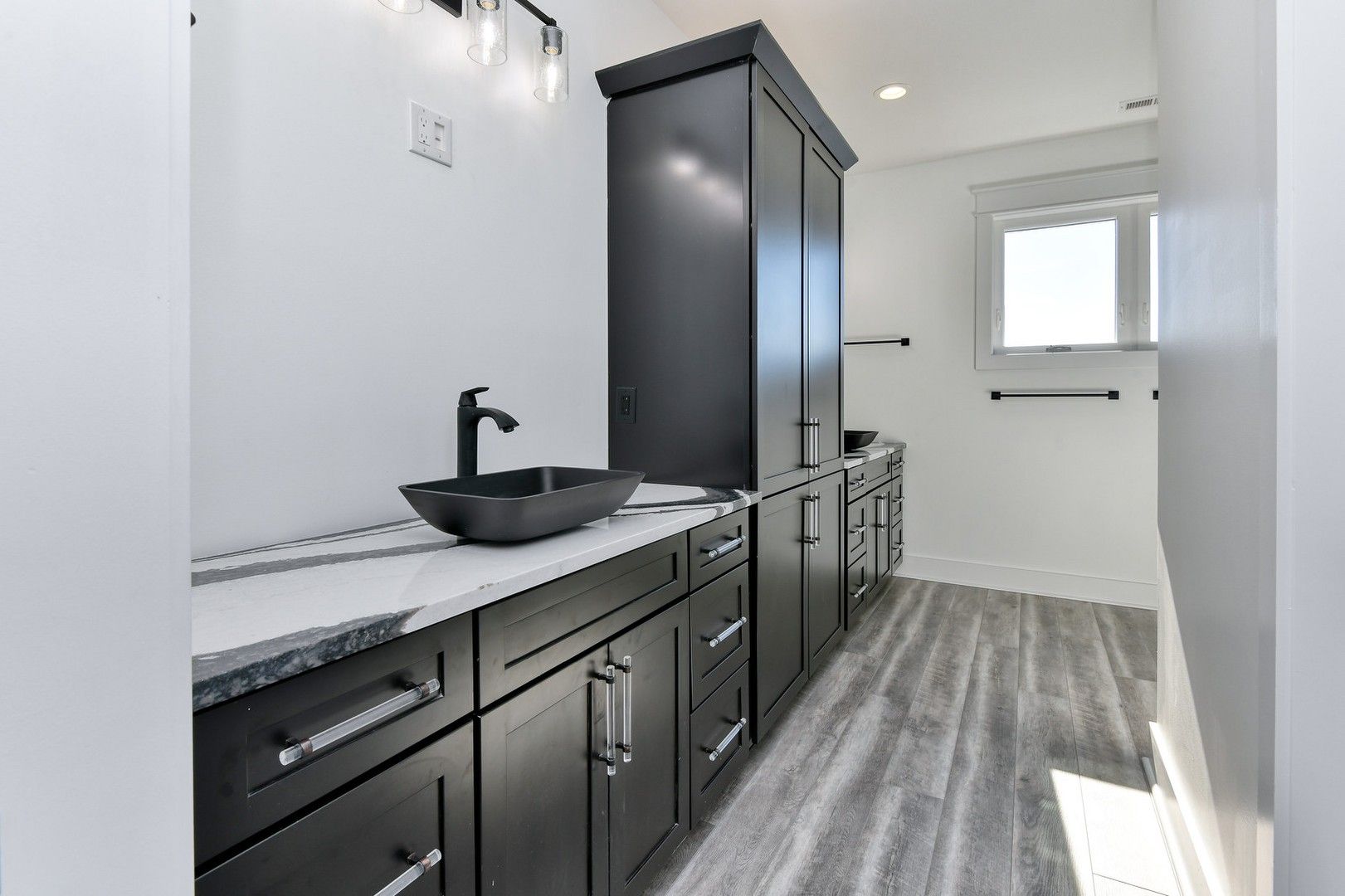 A bathroom with black cabinets , a sink , and a window.
