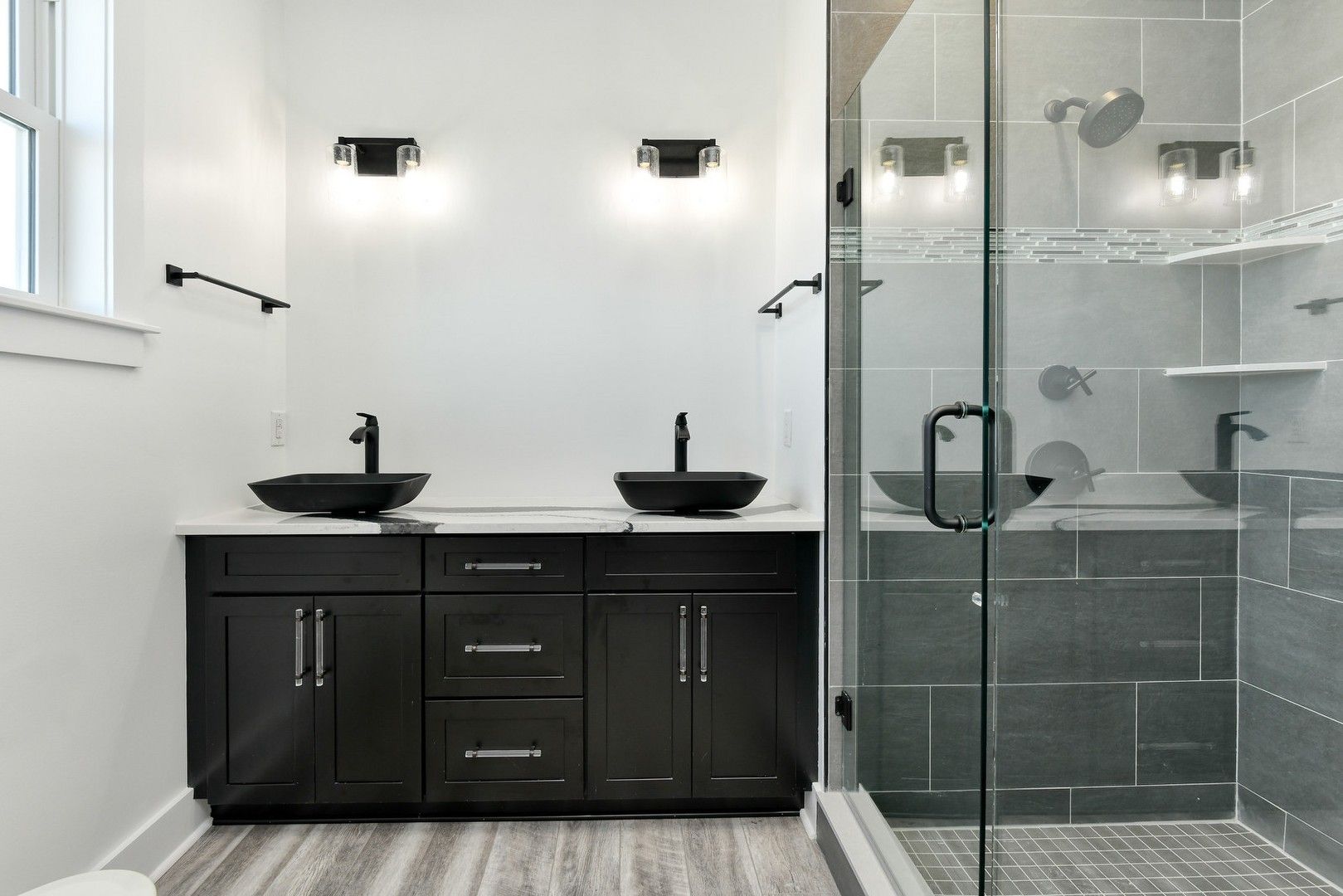 Modern bathroom with black vanity, two sinks, and glass shower.