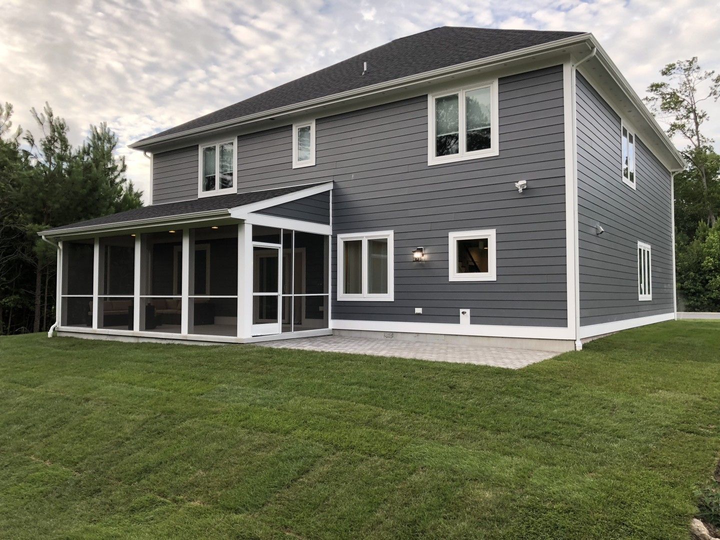 A large gray house with a screened in porch in the backyard.