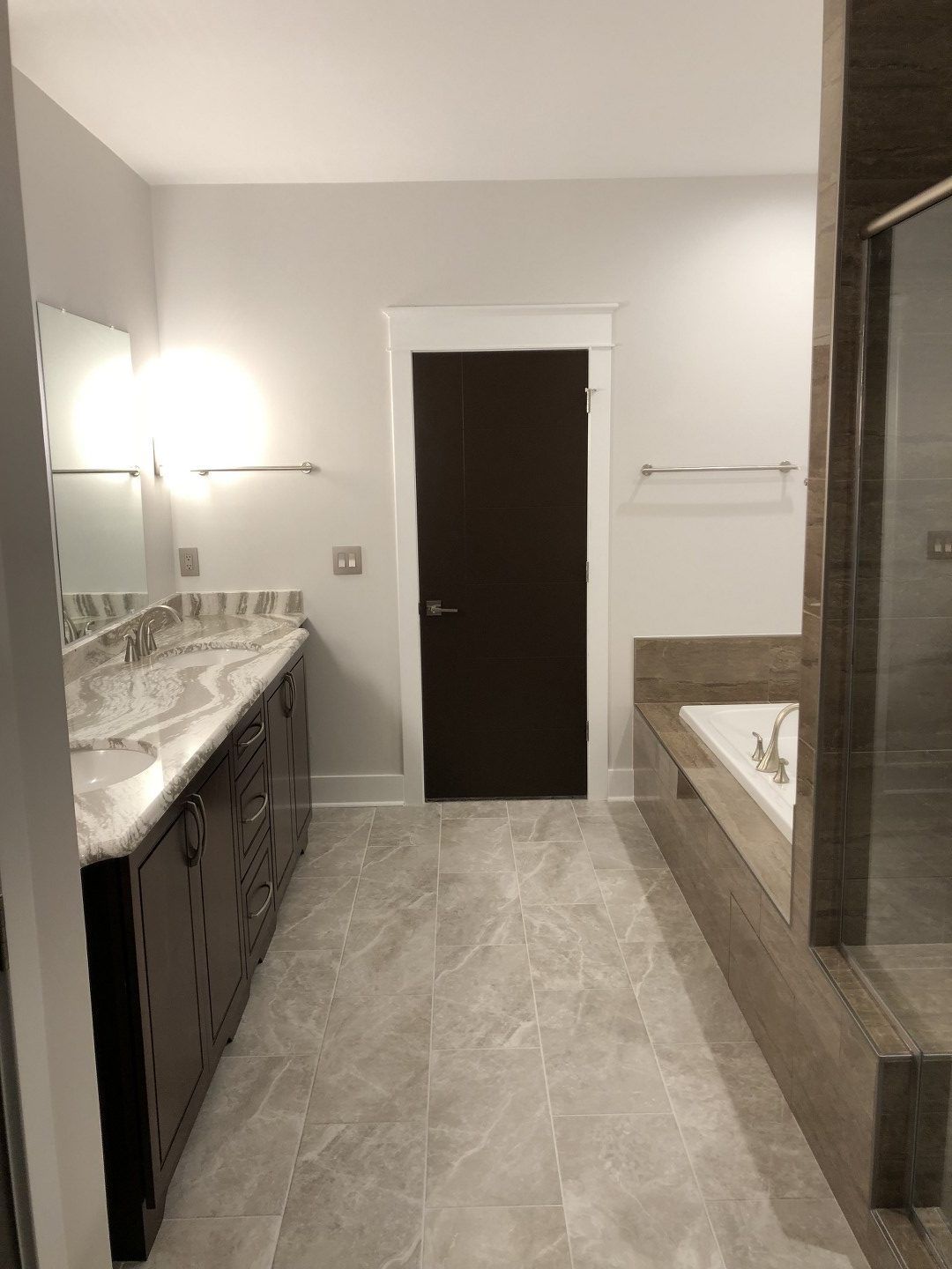 A bathroom with two sinks , a tub , a mirror and a door.