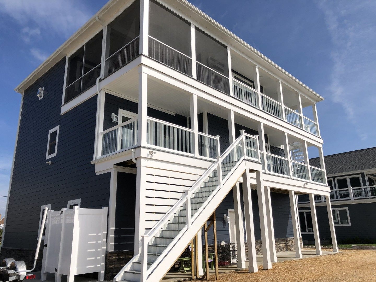 Two-story blue house with white trim, a staircase, and screened-in balconies under a blue sky.