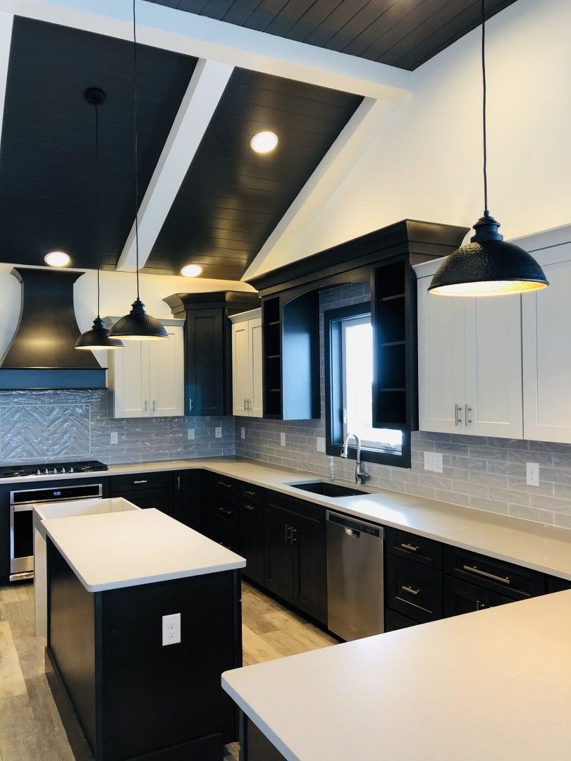 A kitchen with black cabinets , white counter tops , stainless steel appliances and a large island.