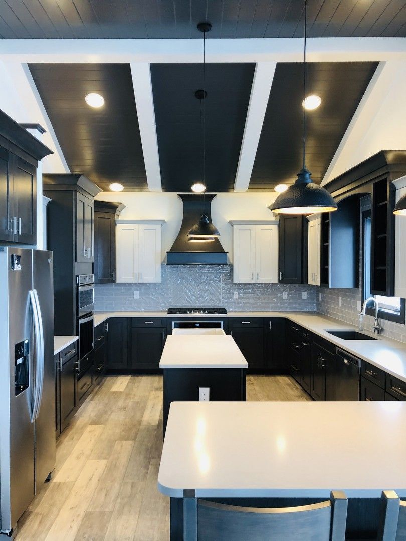 Modern kitchen with black cabinets, white countertops, and a unique ceiling design.