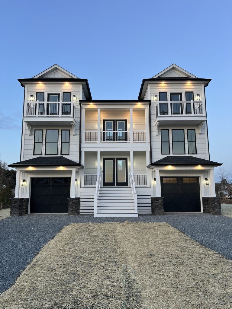 A large white house with black garage doors and stairs