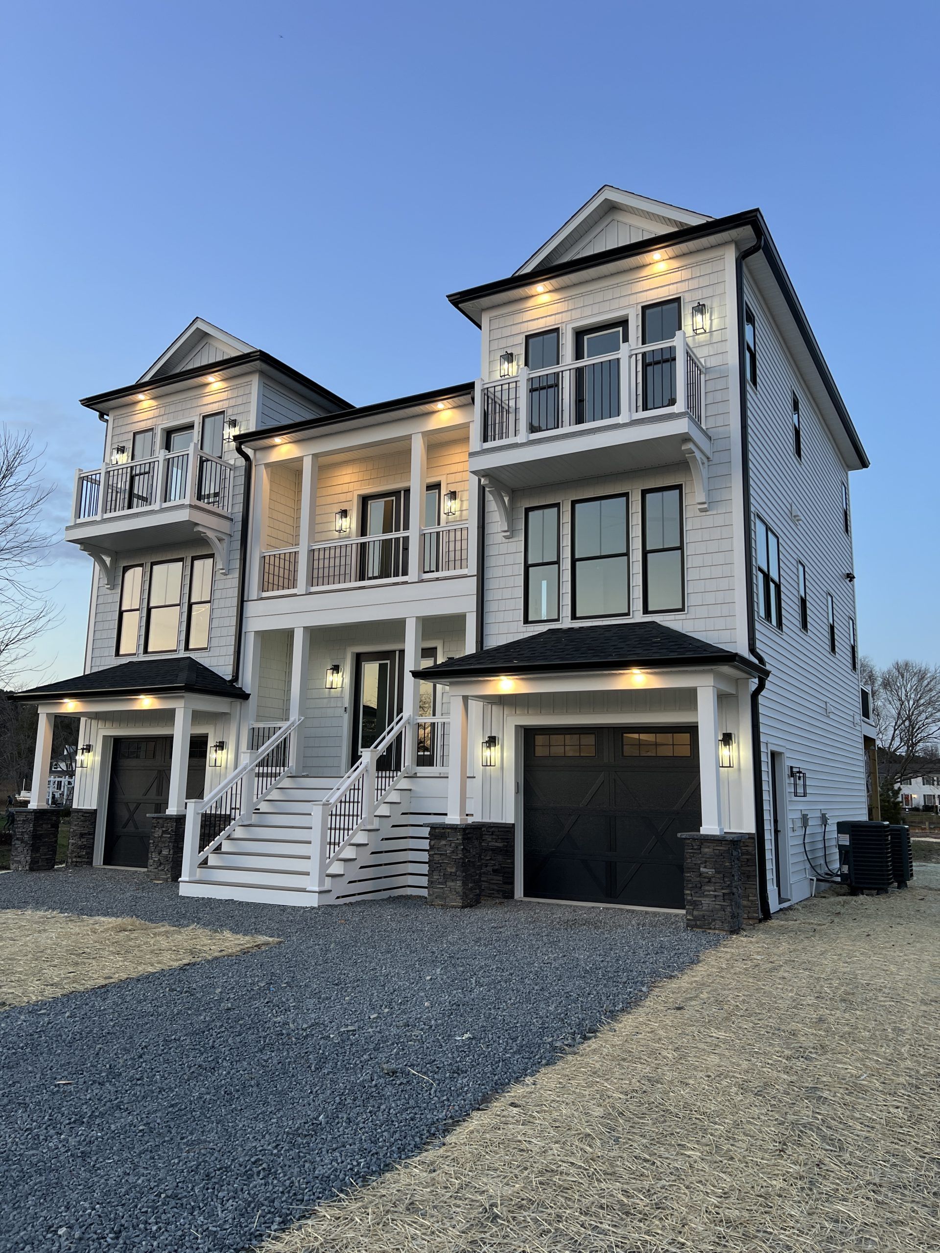 A large white house with black trim is sitting on top of a gravel driveway.