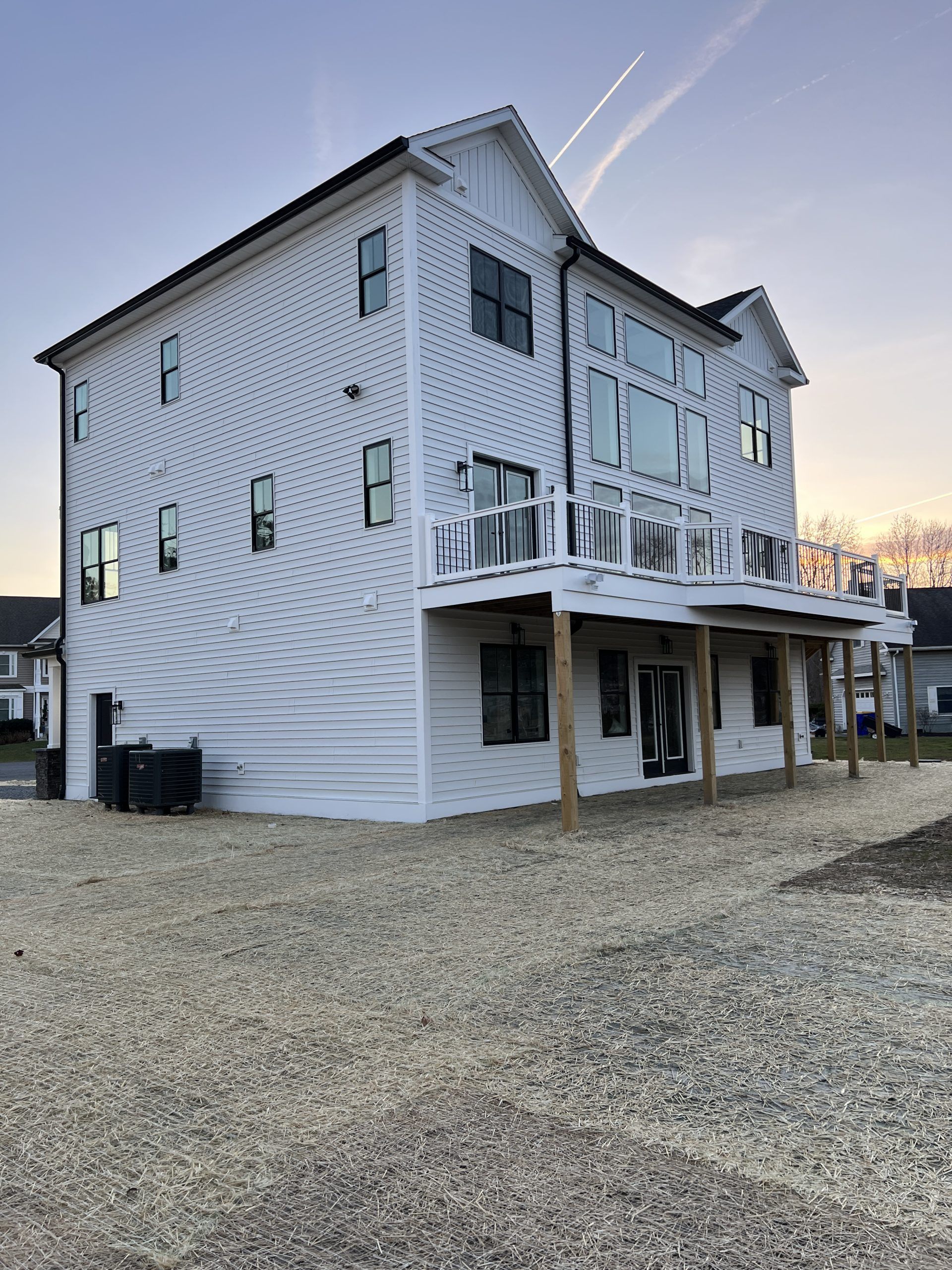 A large white house with a large deck is sitting on top of a gravel lot.