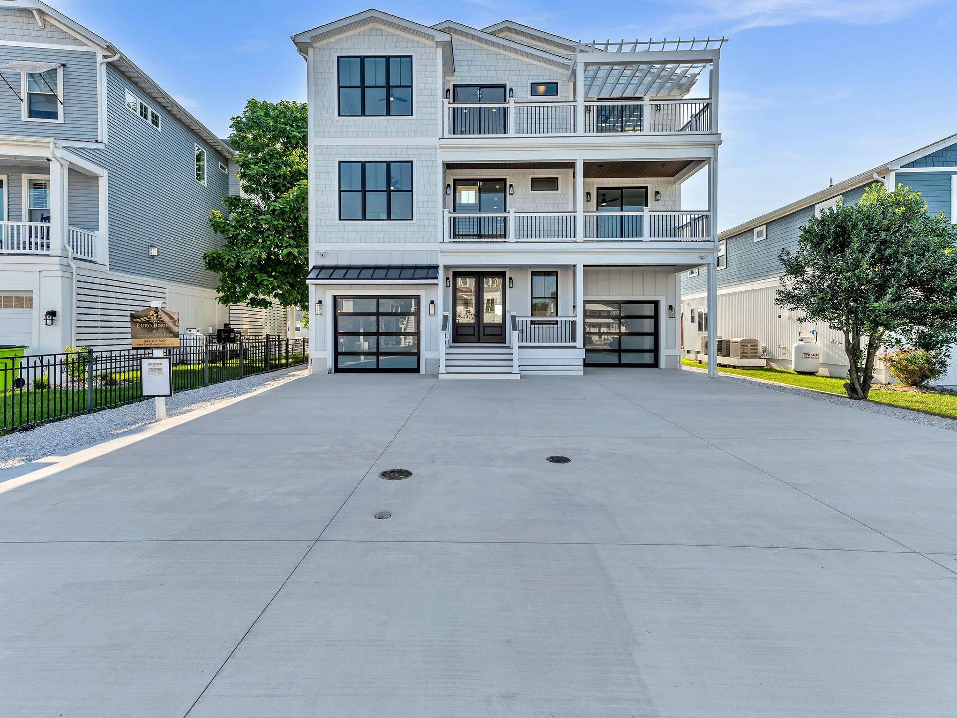 Modern three-story house with light gray siding, balconies, glass garage doors, and a large concrete driveway.