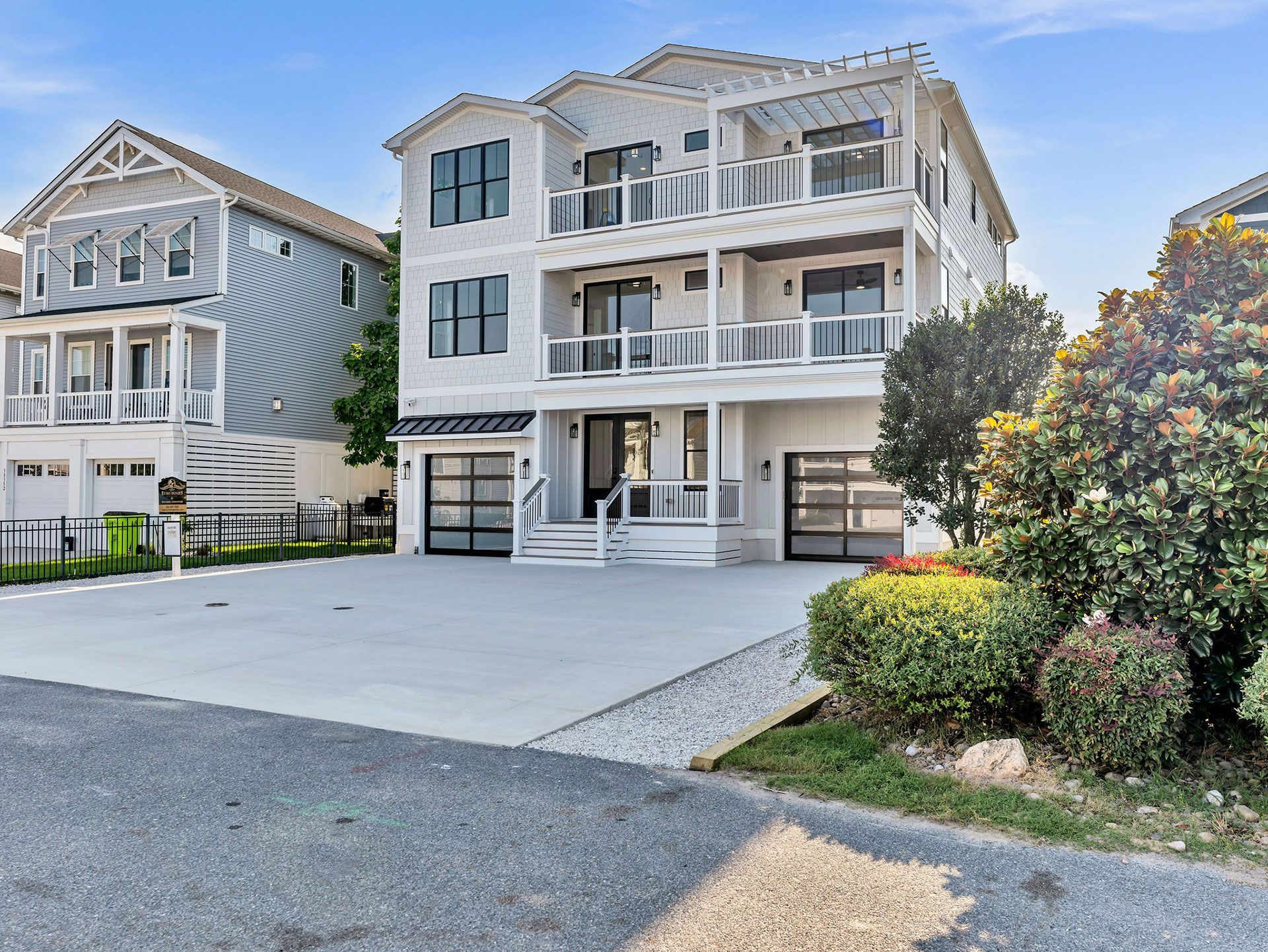 Three-story white house with balconies, garage doors, and black window frames, in front of a driveway.
