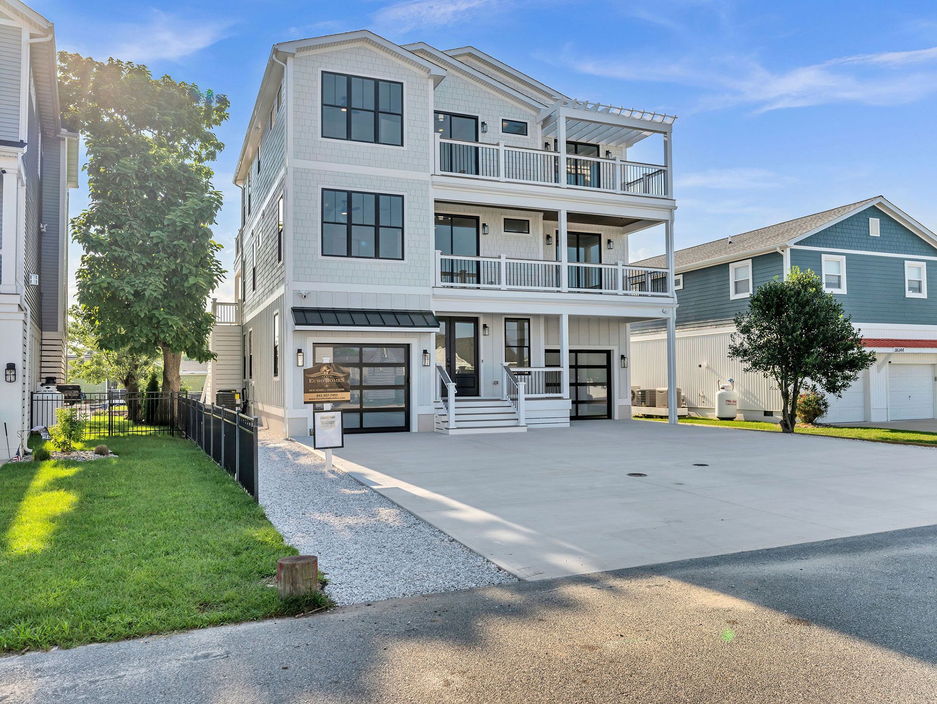 Modern house with multiple balconies and garage. Exterior is white with black accents, in a sunny setting.
