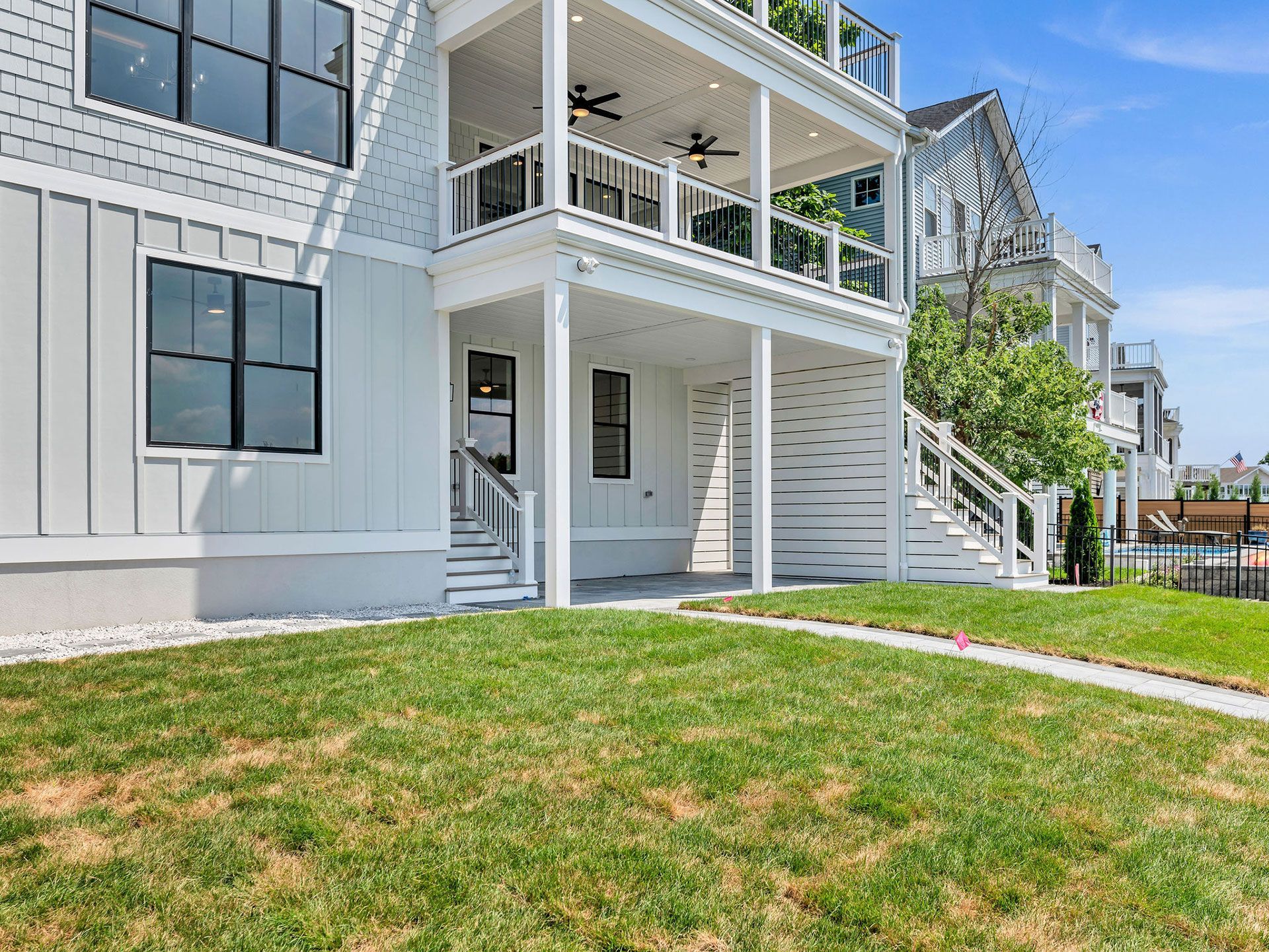 White multi-story house with balconies and stairs on a green lawn, with a blue sky background.