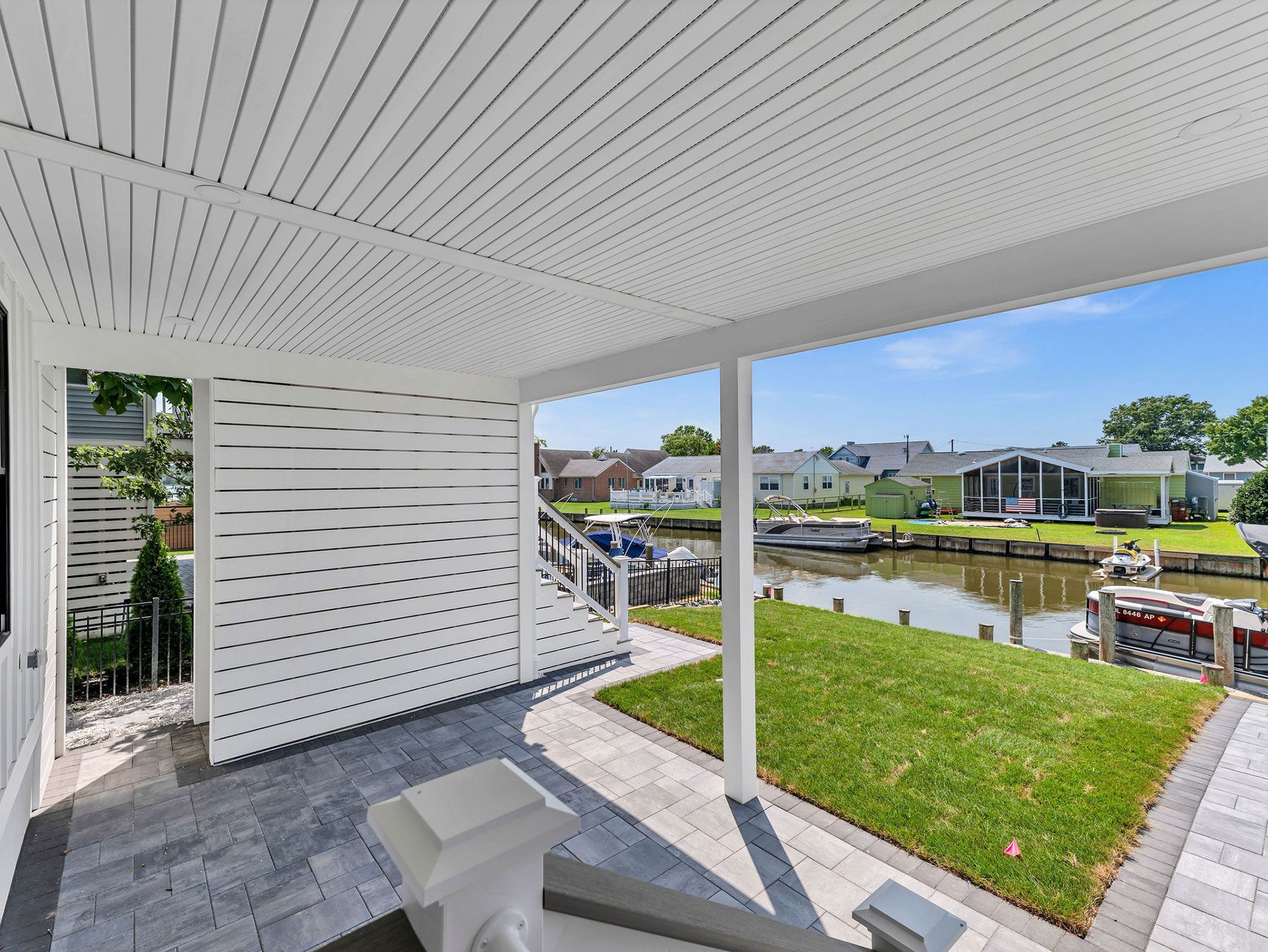 Covered porch overlooking a canal with green grass and houses. White and gray colors dominate.