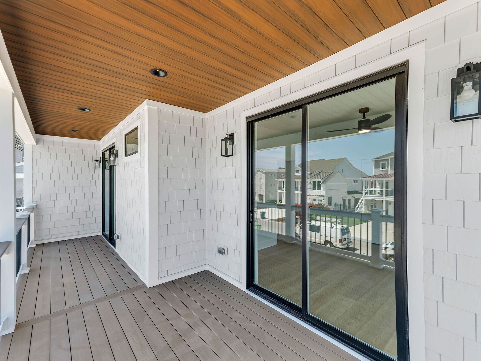 Covered porch with white shingle siding, sliding glass door, dark trim, and wooden ceiling.