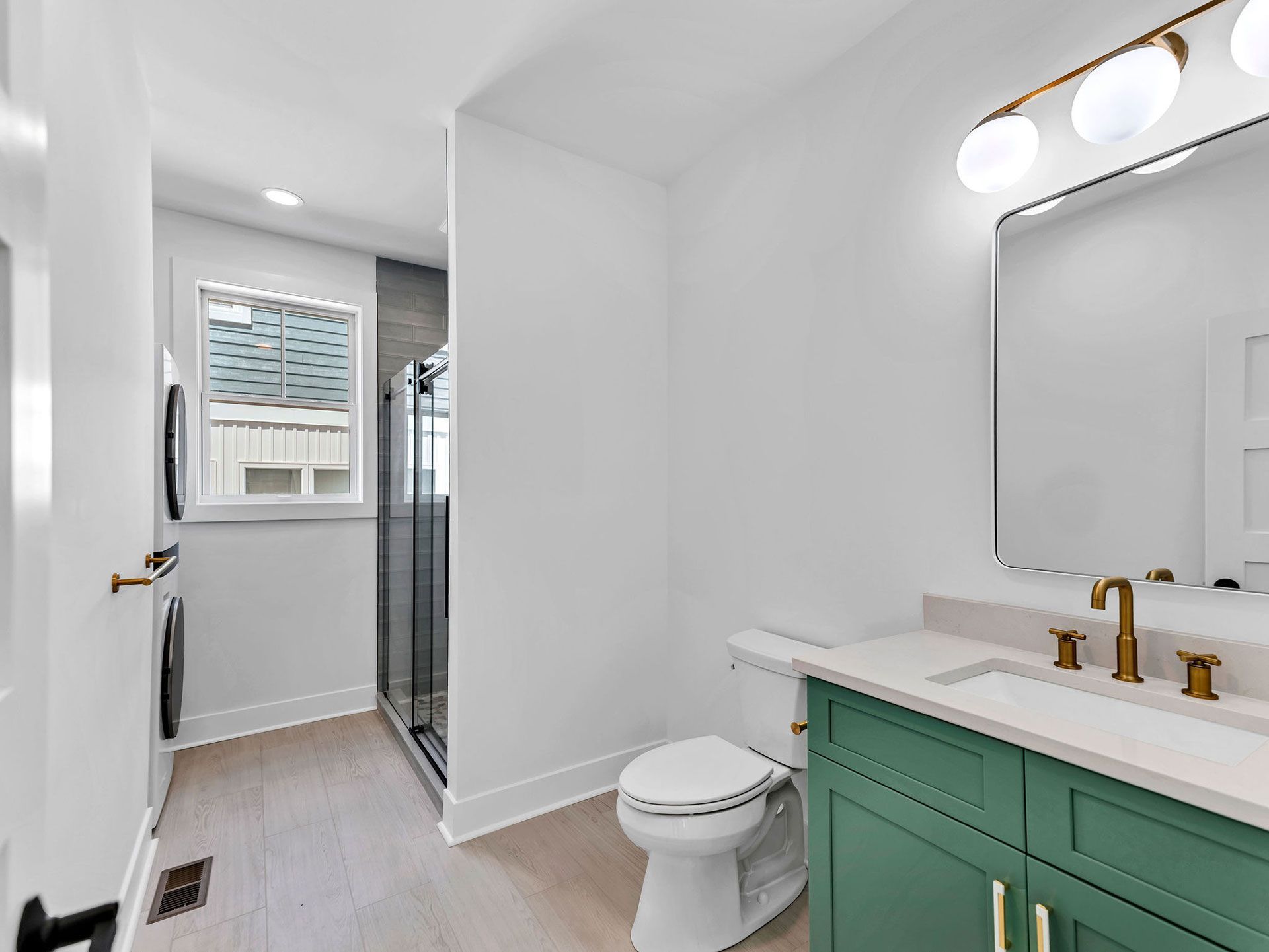 Modern bathroom with green vanity, gold fixtures, and light wood floors.