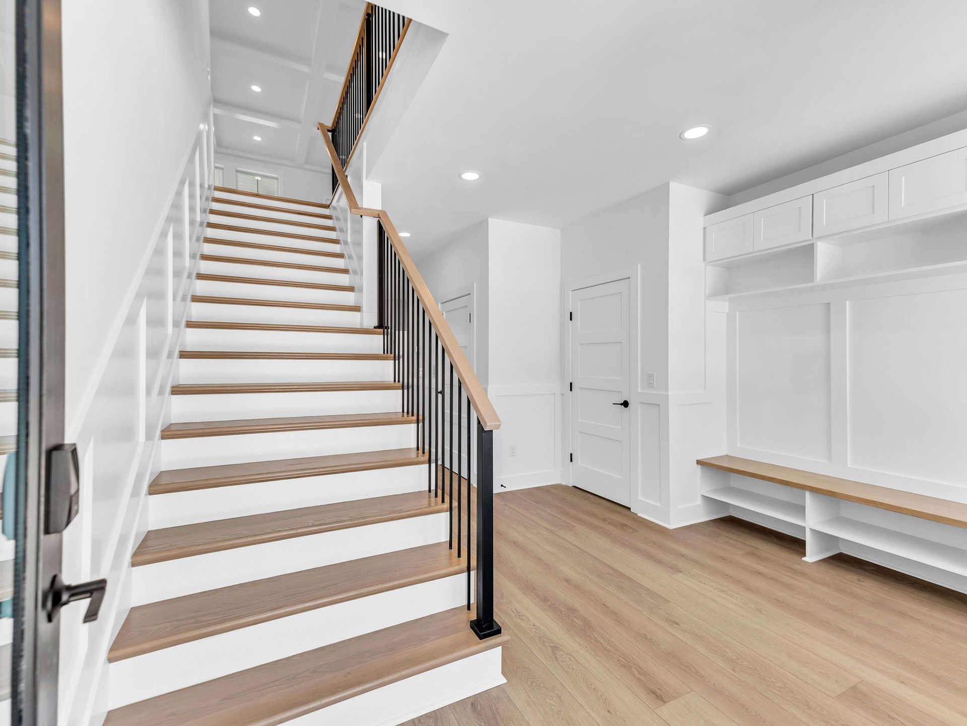 Hallway with stairs and built-in bench. Light wood floors and steps, white walls, black and wood railing.