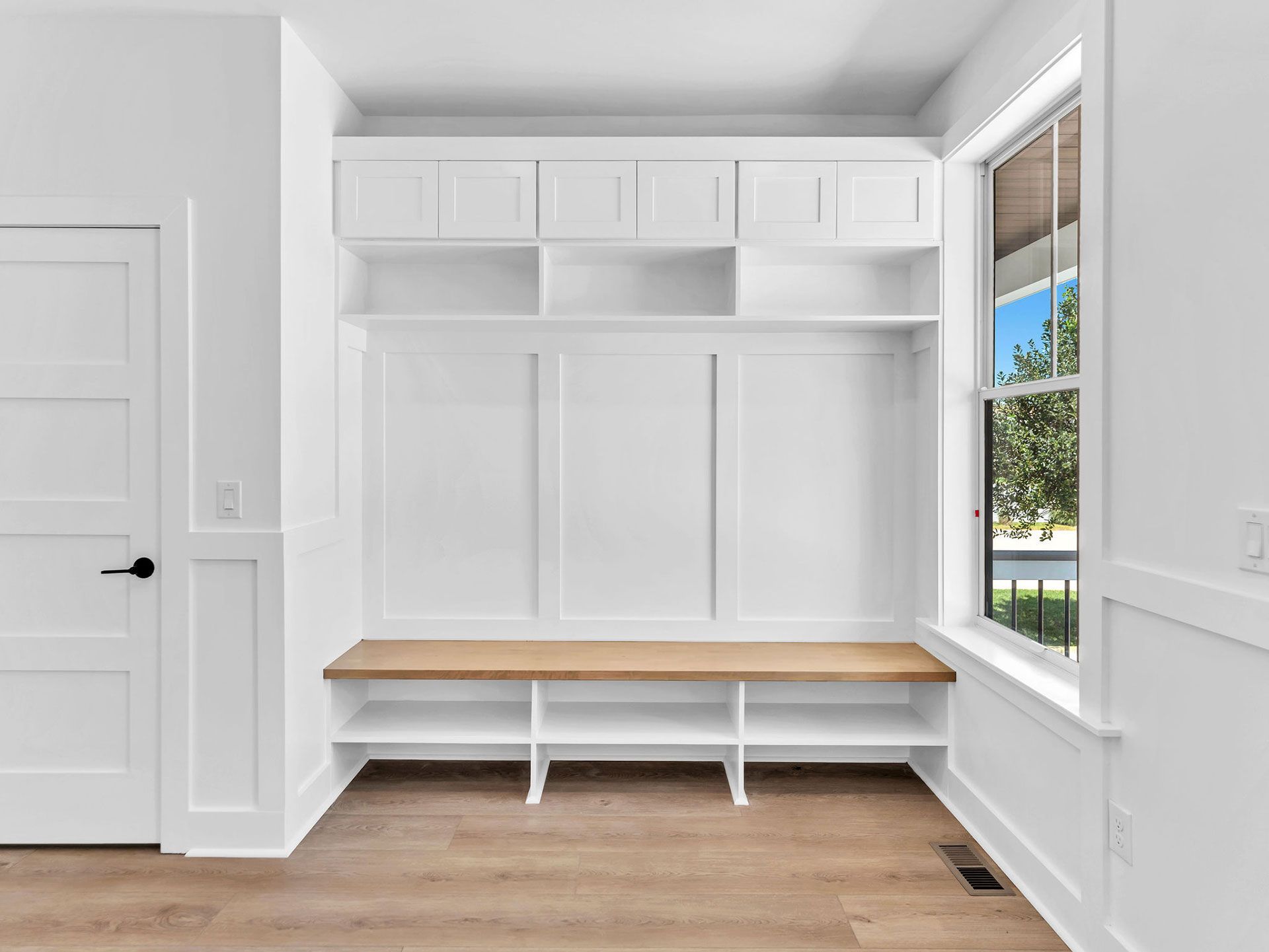 White built-in entryway storage with a bench, cabinets, shelves, and a window.
