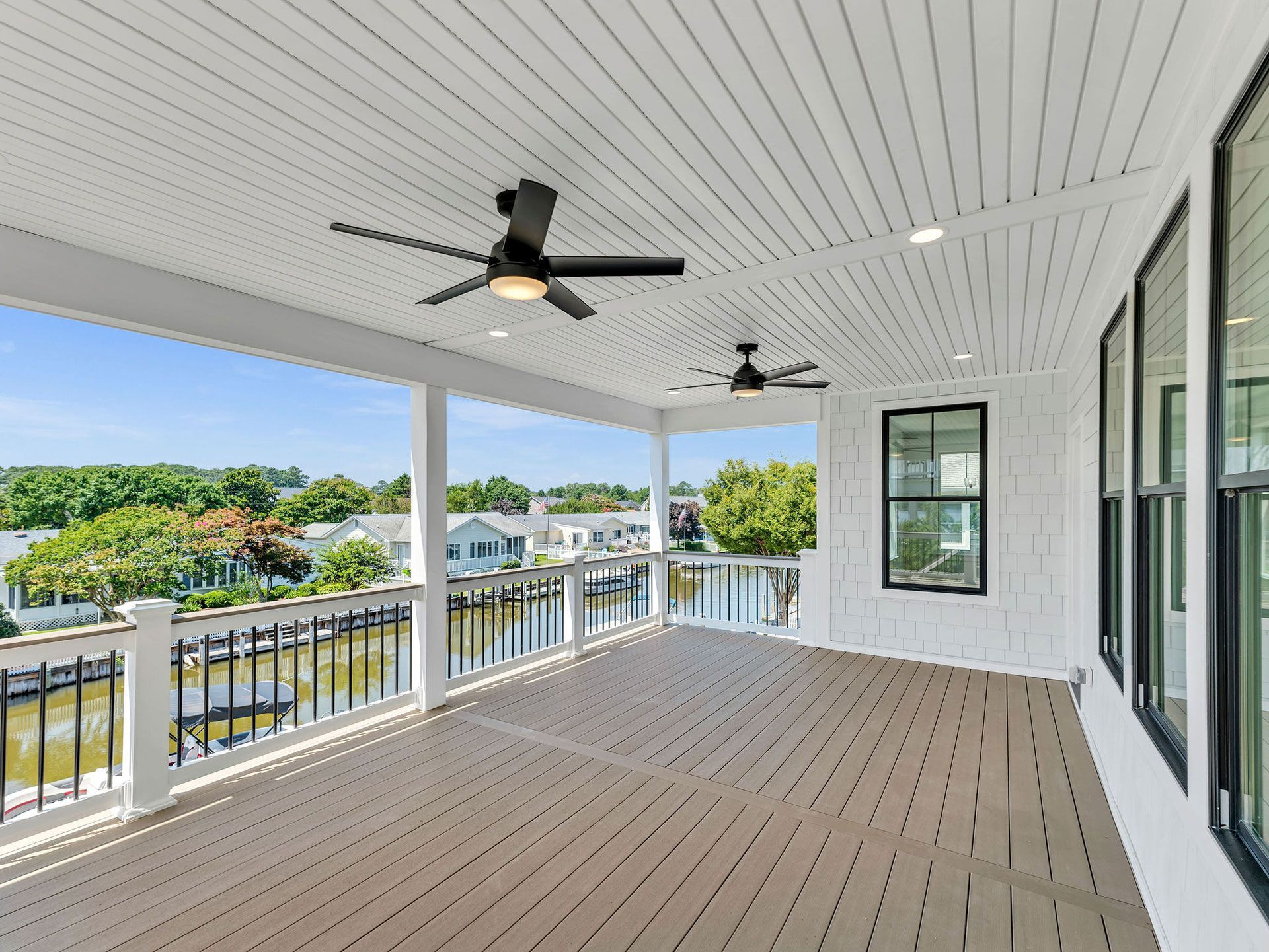 Covered deck overlooking waterway with white trim, black ceiling fans, and windows.