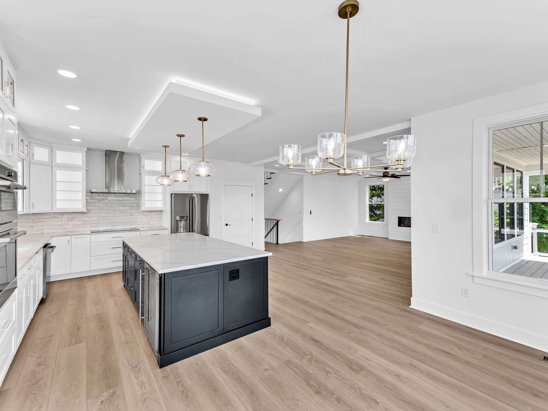 Modern kitchen with white cabinets, dark island, wood floors, and a chandelier.