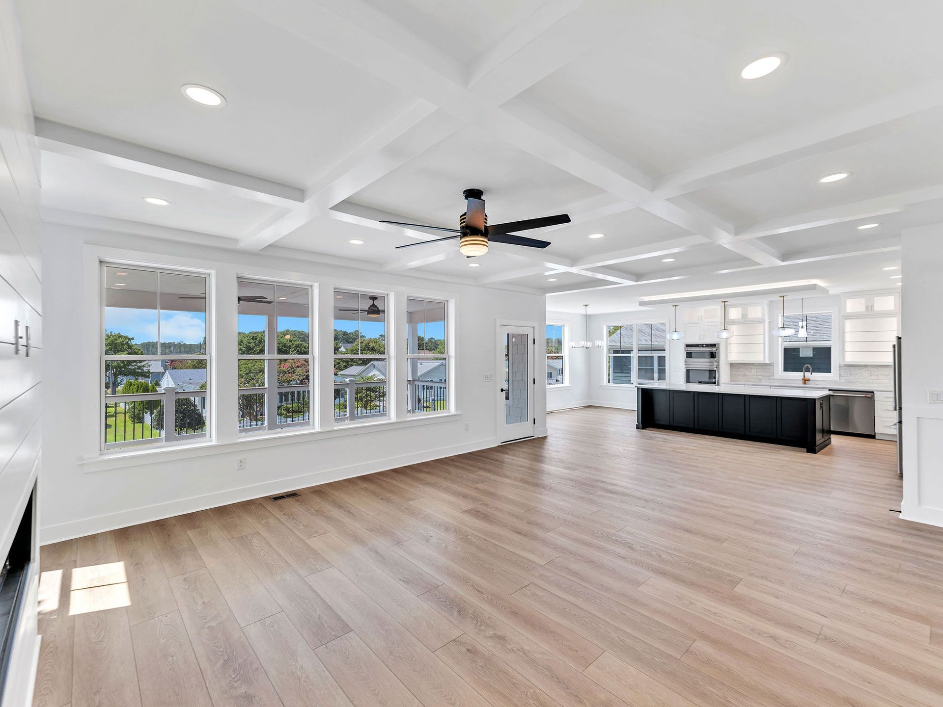 Bright, modern living room with light wood floors, coffered ceiling, and large windows overlooking a sunny view.