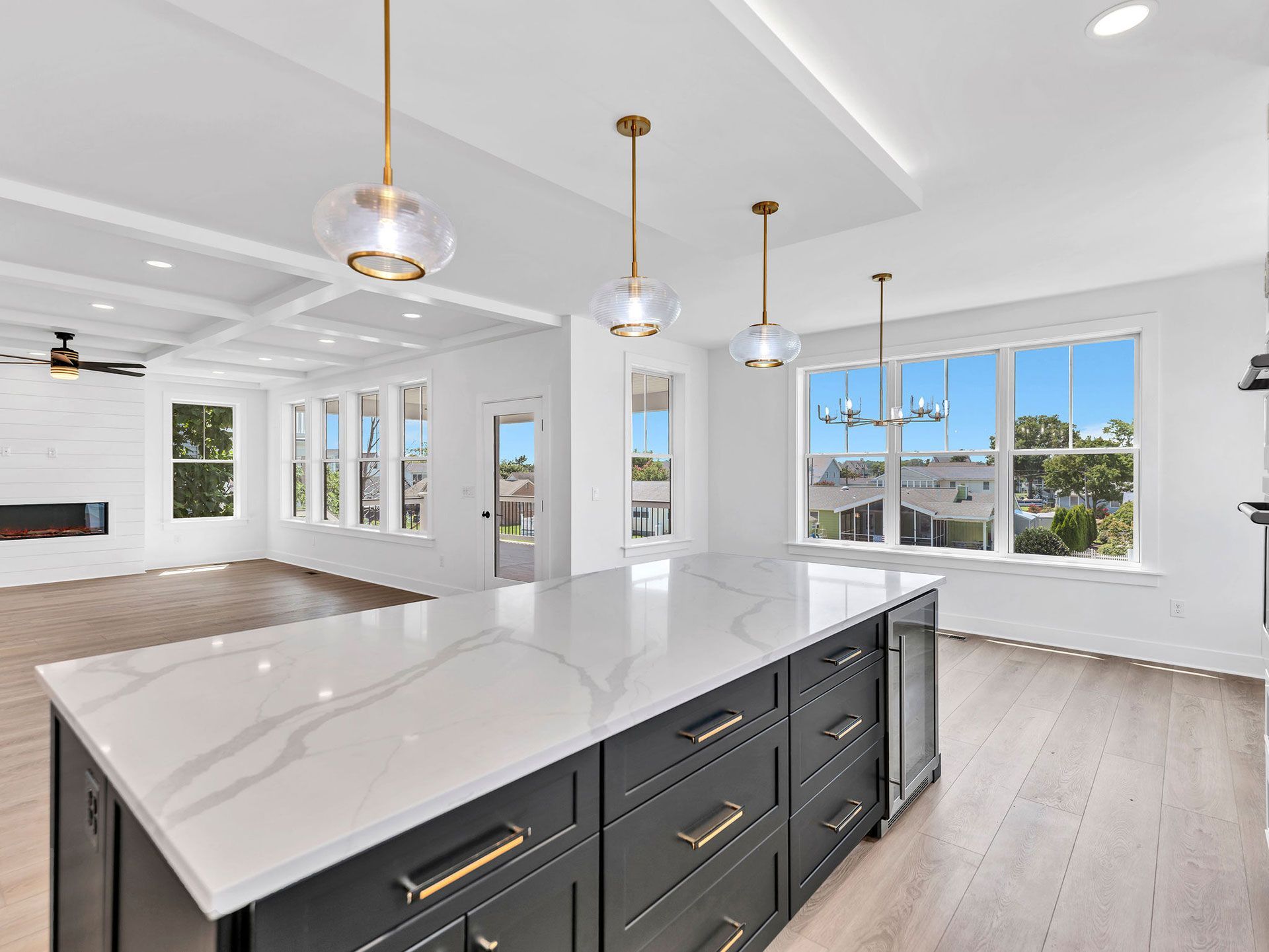 Kitchen with large island, dark cabinets, white countertop. Gold pendant lights, hardwood floor, large windows.