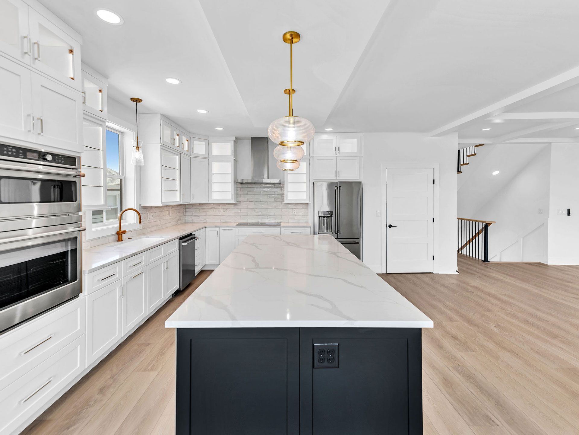 Modern kitchen with white cabinets, dark island, and gold pendant light.