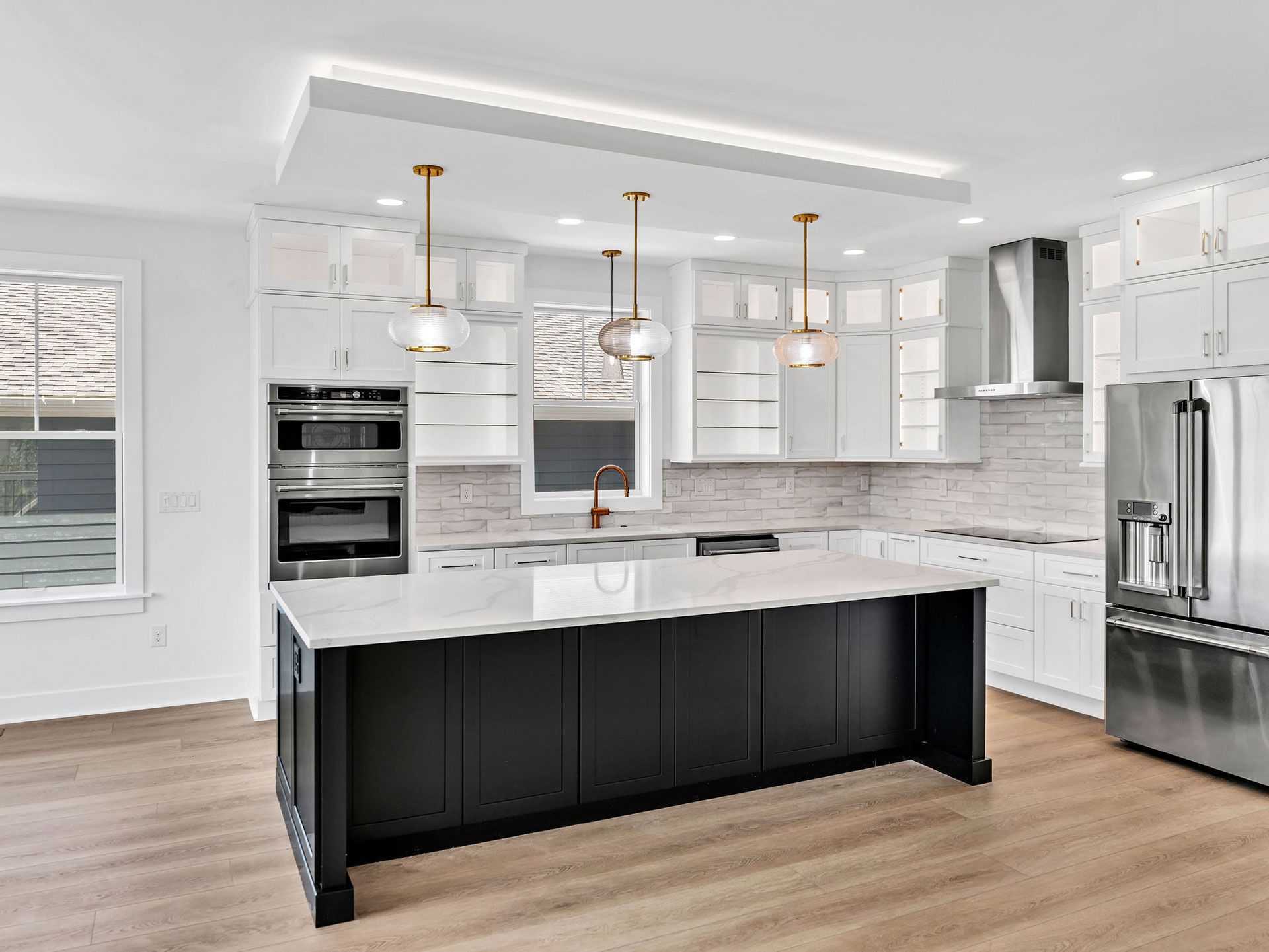 Modern kitchen with black island, white cabinets, stainless steel appliances, and gold pendant lights.