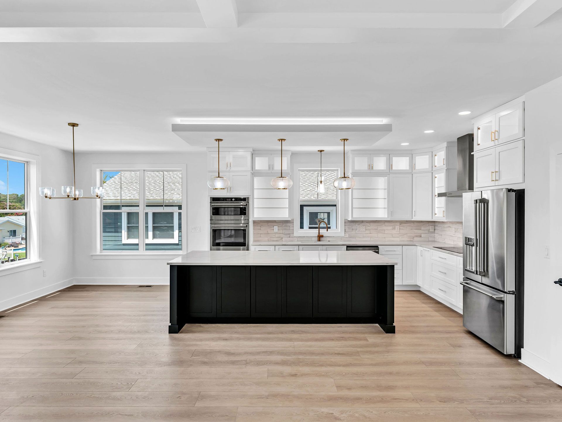 Modern white kitchen with black island, stainless steel appliances, and light wood floors.