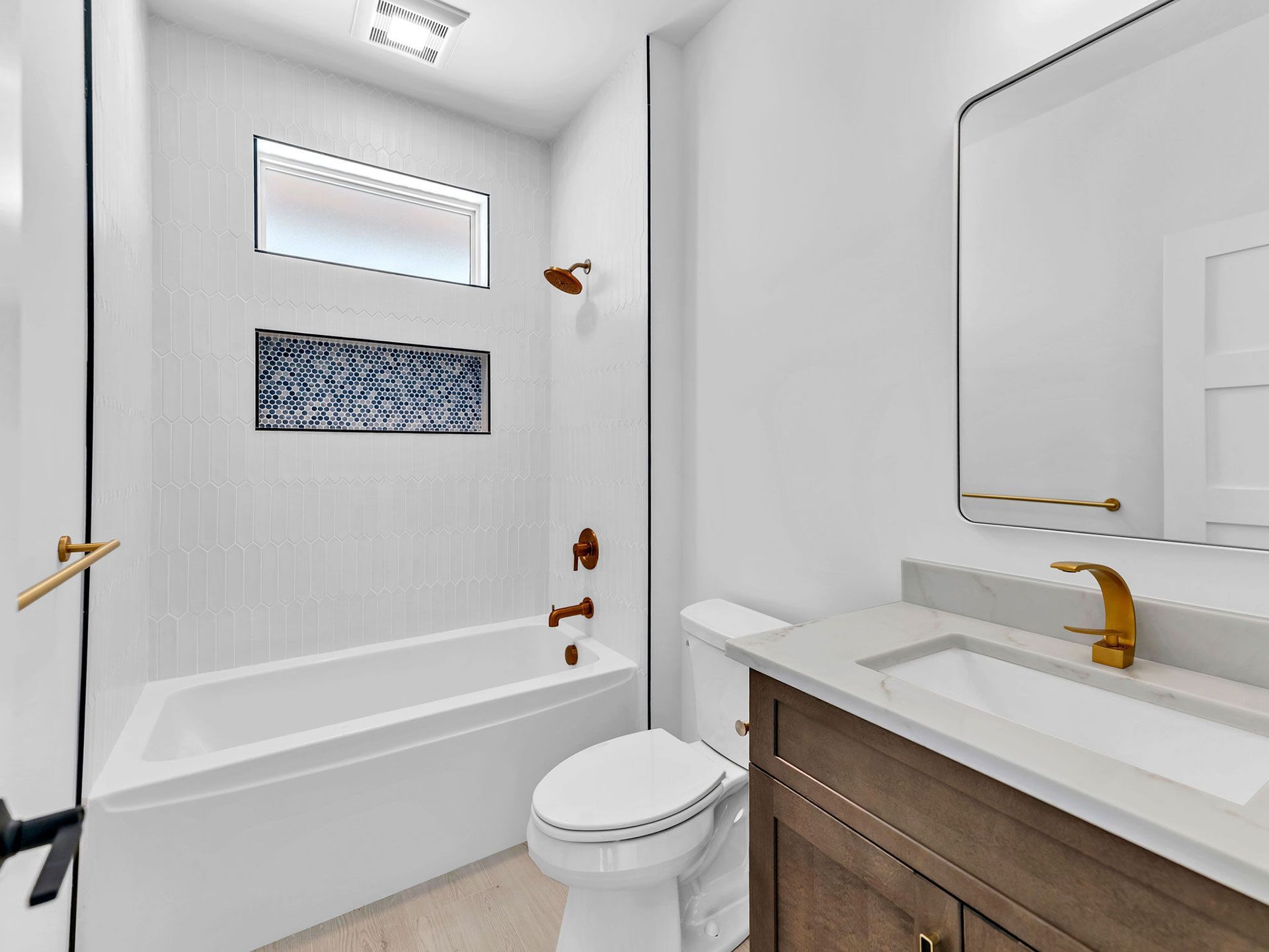 Modern white bathroom with bathtub, toilet, vanity, and gold fixtures.