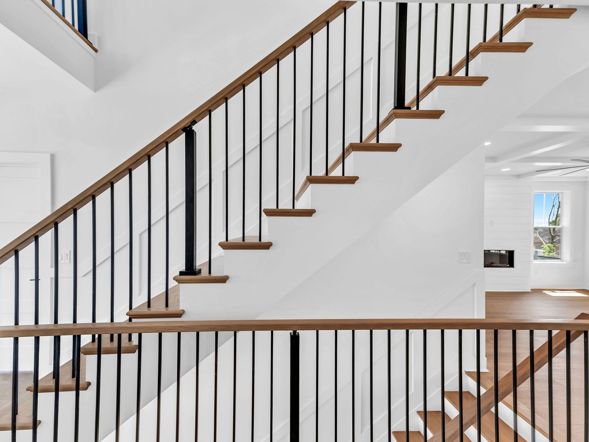 Staircase with wood steps, black metal railings, and white walls.