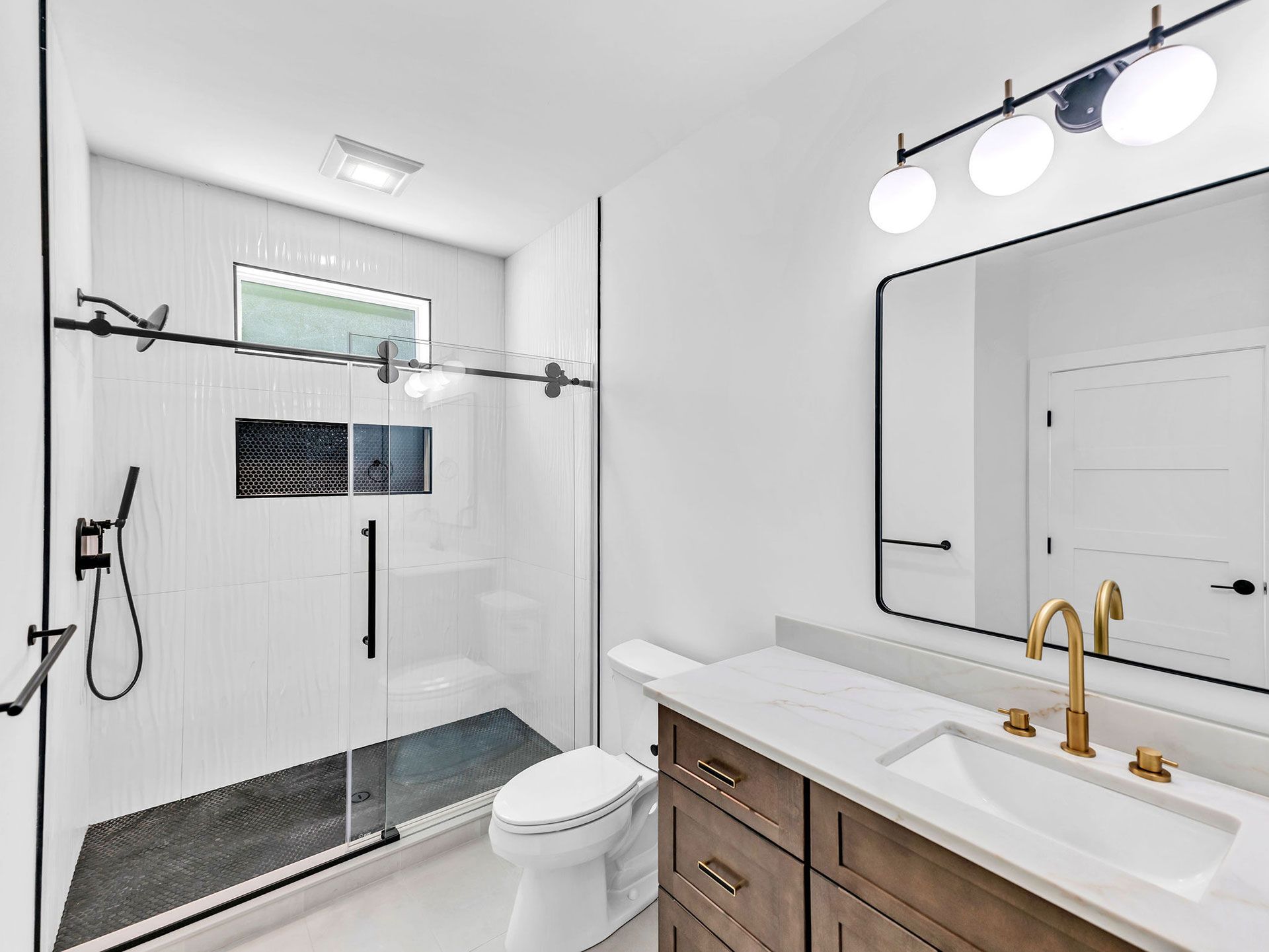 Modern bathroom with white walls, glass shower, wooden vanity, and gold fixtures.