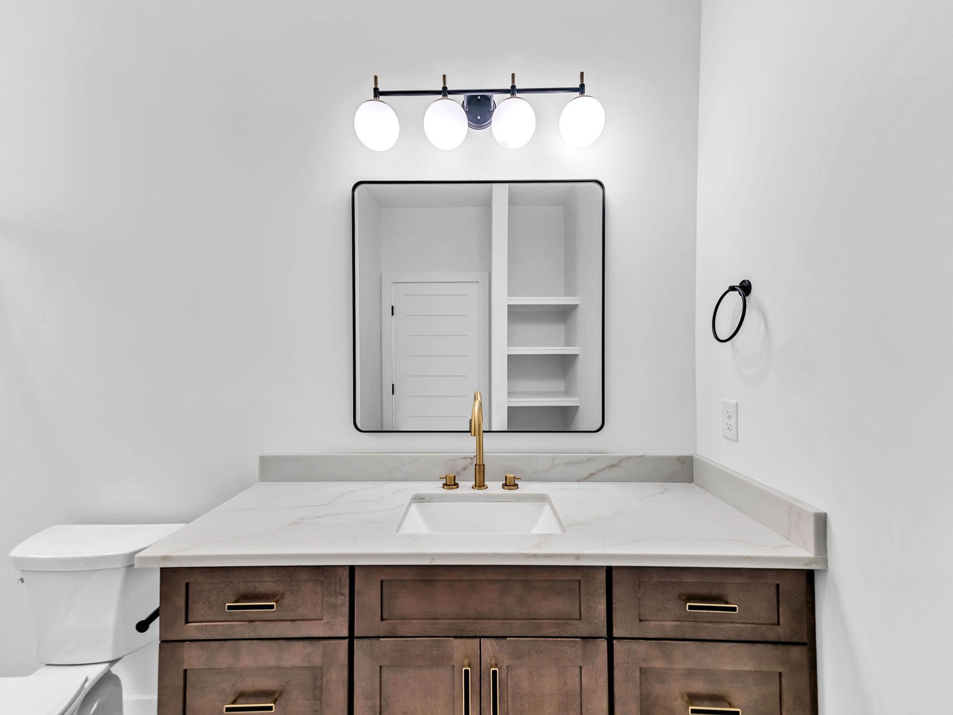 Bathroom with brown vanity, marble countertop, and a black framed mirror with spherical lights above.