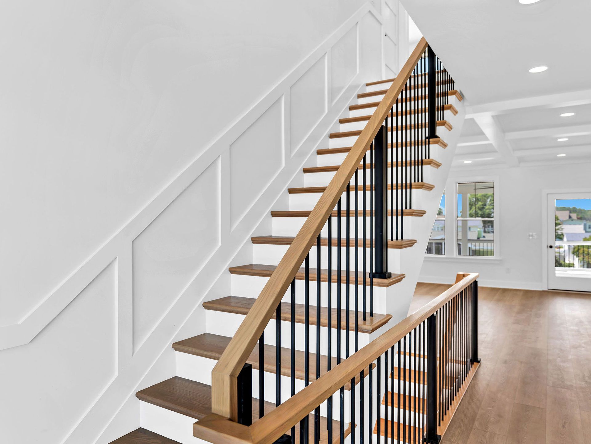 Wooden staircase with white paneling, black railings, and wood handrails in a well-lit home.